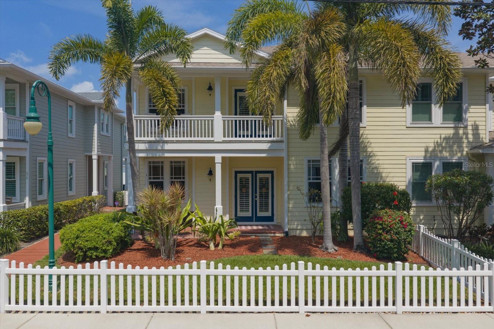 Front of unit, fenced front yard, large covered patio, brick walkway, French doors, palm trees
