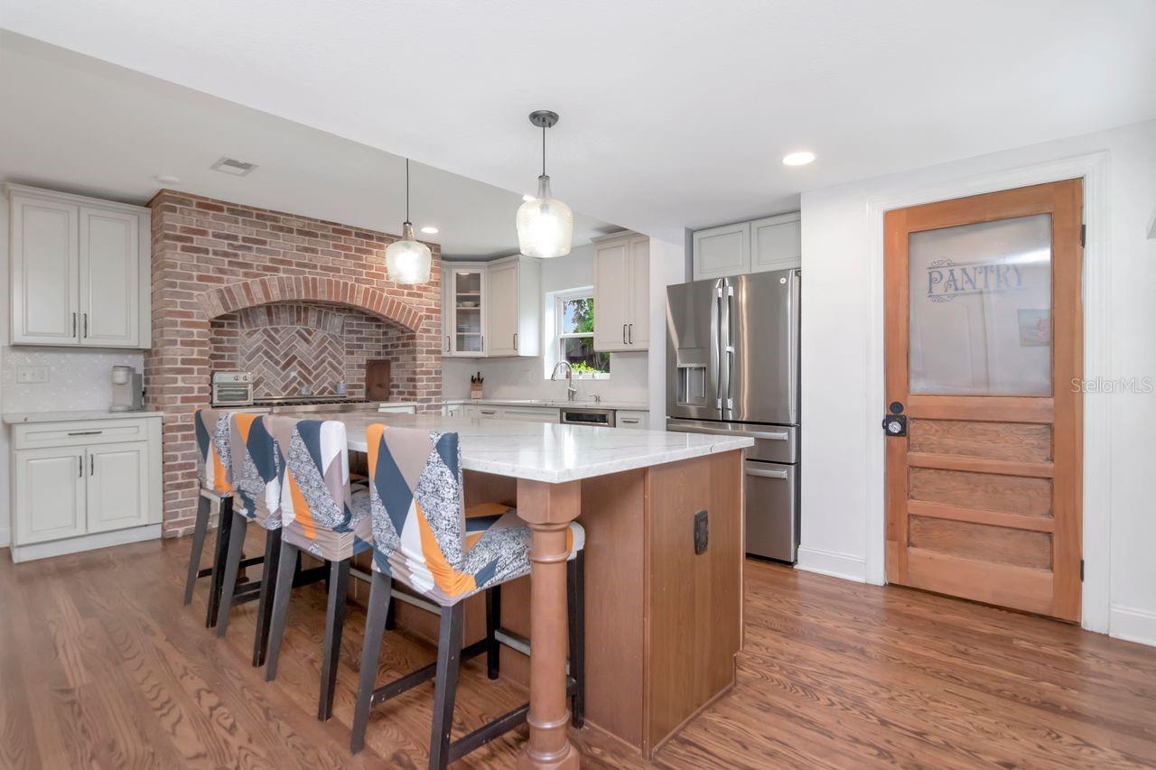 Chef's Kitchen with Statement Brick Alcove for the High-End Gas Range. Plenty of Cabinet Space, Pendant Lighting over the Island Undermount Sinkm and Custom Pantry Door and Hardwood Floors.