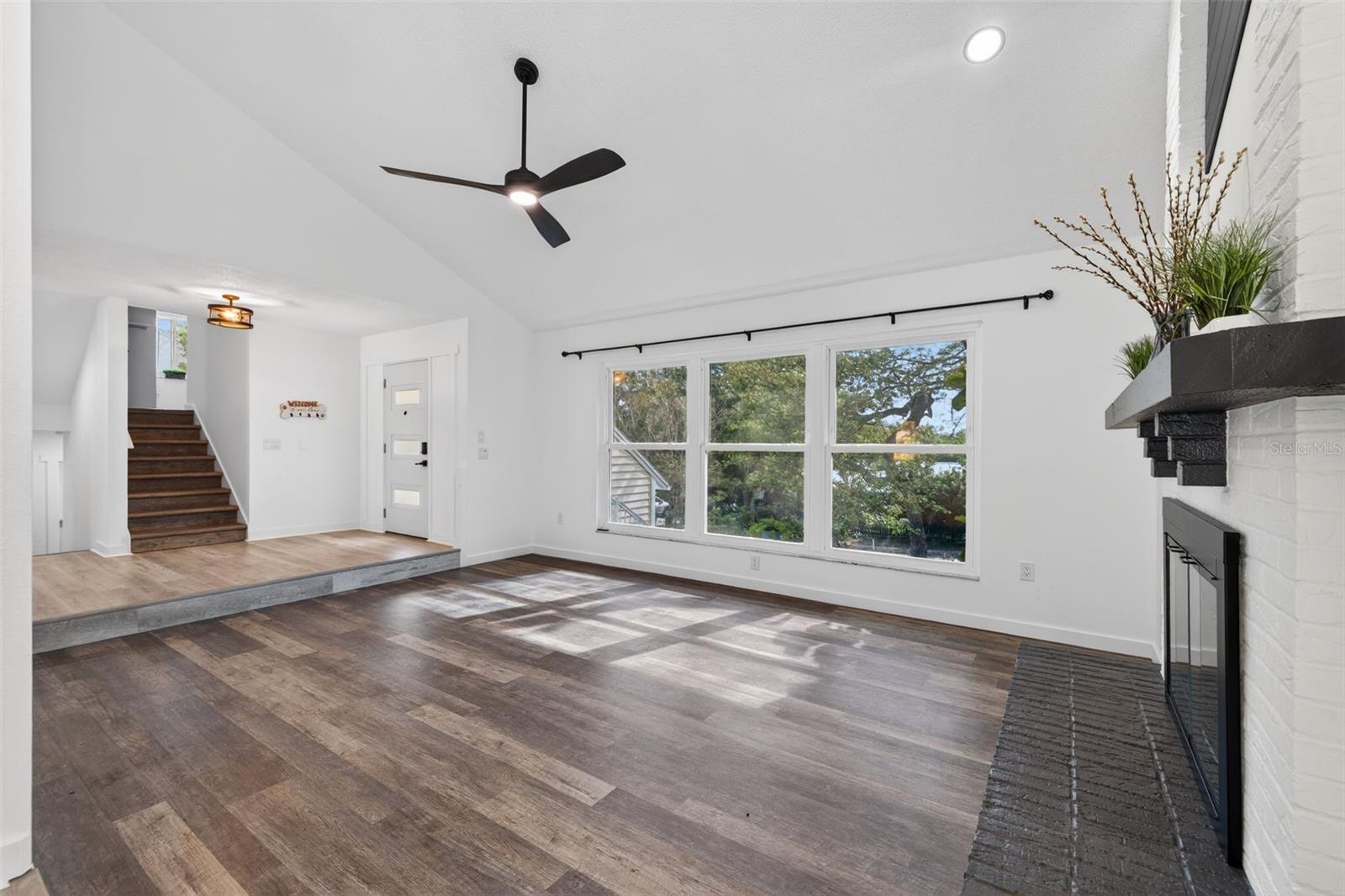 The main living area features vaulted ceilings with decorative beams, a wood-burning fireplace, and large hurricane-rated windows that fill the space with natural light.
