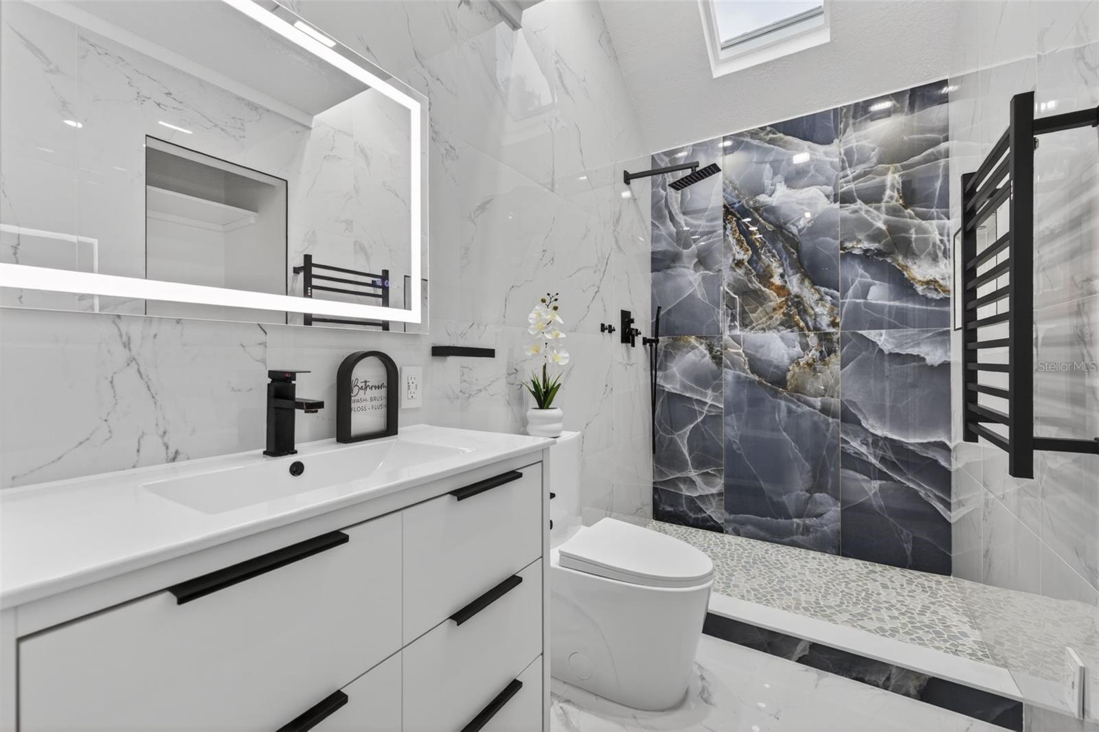 Full remodeled bathroom with beautiful tile, built-in shelving, and a lighted mirror. A heated towel rack adds comfort and functionality. The skylight adds natural light.