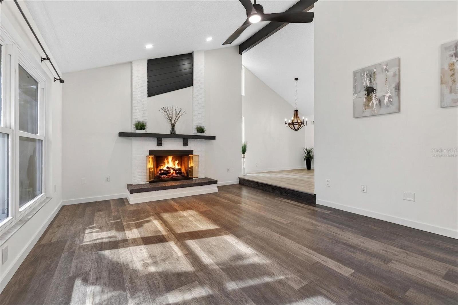 The main living area features vaulted ceilings with decorative beams, a wood-burning fireplace, and large hurricane-rated windows that fill the space with natural light. Fire was virtually staged.