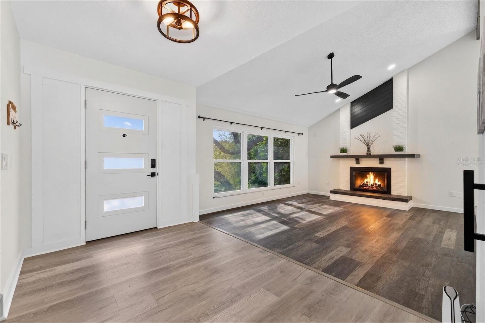 The main living area features vaulted ceilings with decorative beams, a wood-burning fireplace, and large hurricane-rated windows that fill the space with natural light. Fire was virtually staged.