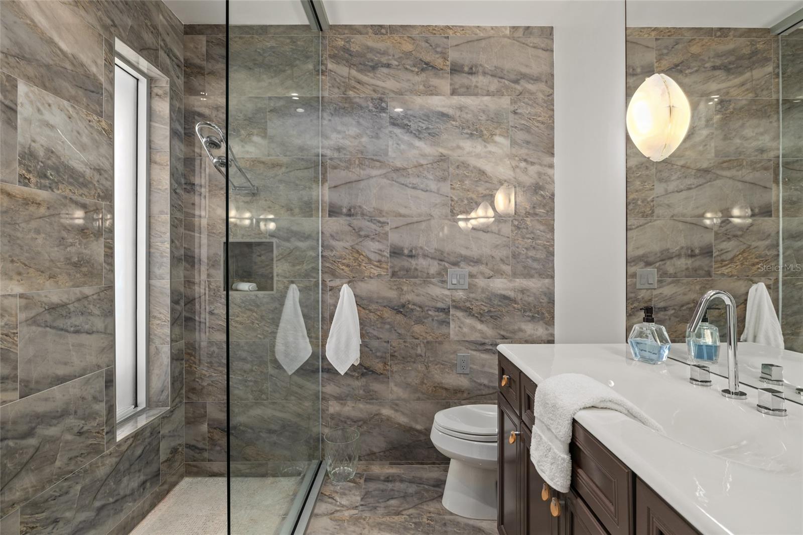 Stylish en suite bath with glass shower and contemporary stone finishes