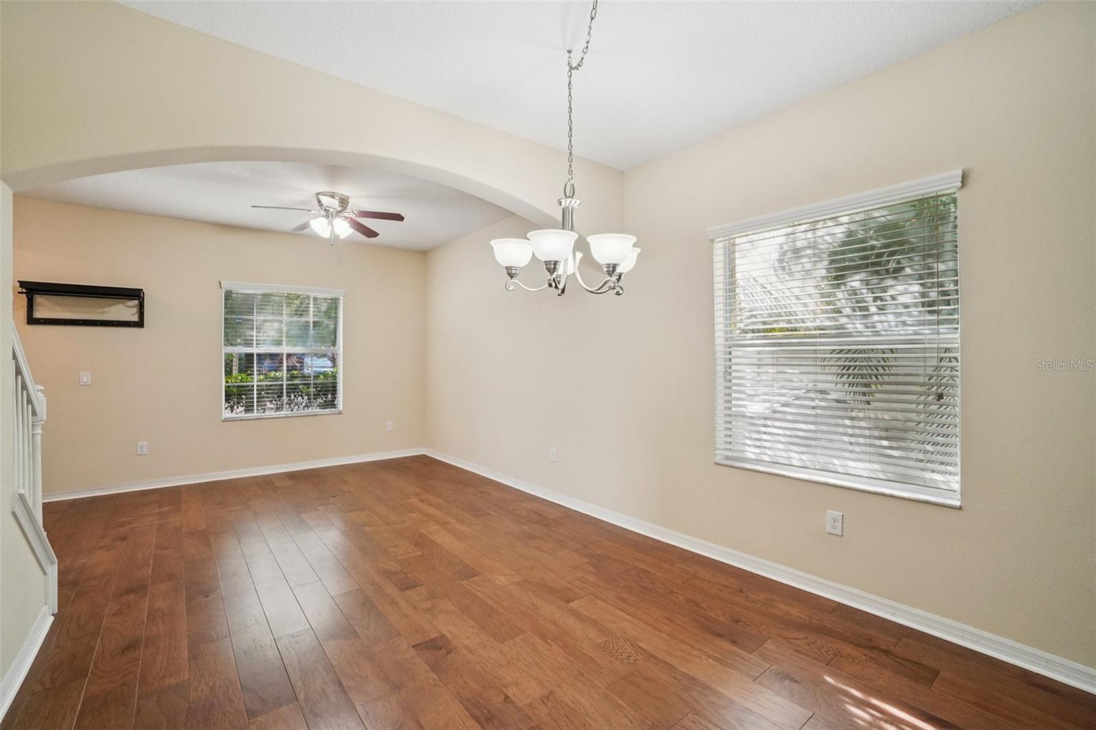 Dining Room / Flex Space - This bright, open room features gleaming hardwood floors, a chandelier, ceiling fan, and two windows that bathe the space in natural light — a versatile area suitable as a formal dining room or sitting room.