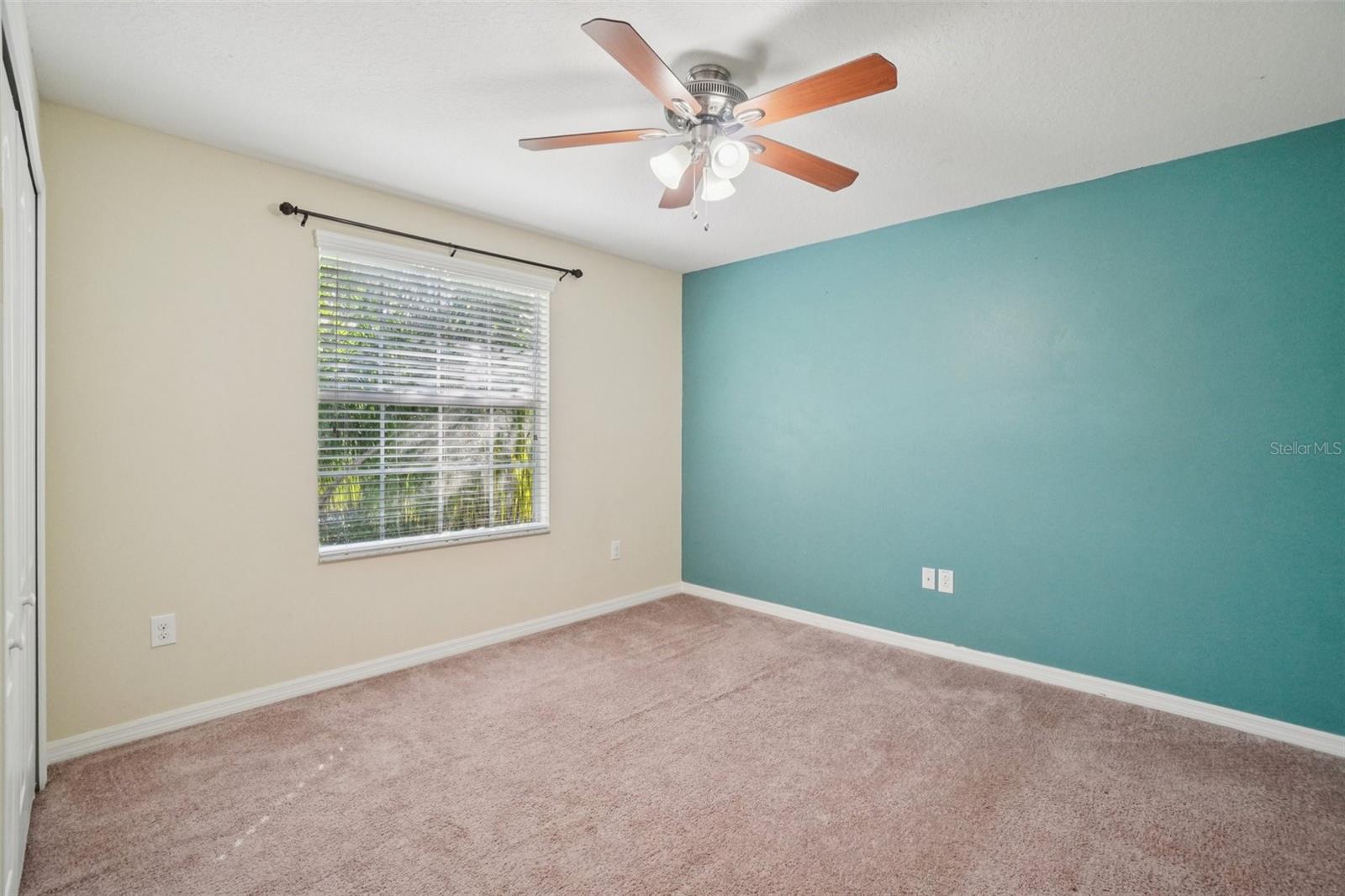 Fourth BedroomThis bright fourth bedroom features plush carpet, a ceiling fan, a window with lush tropical views, and a teal accent wall — a cheerful and comfortable space with plenty of natural light.