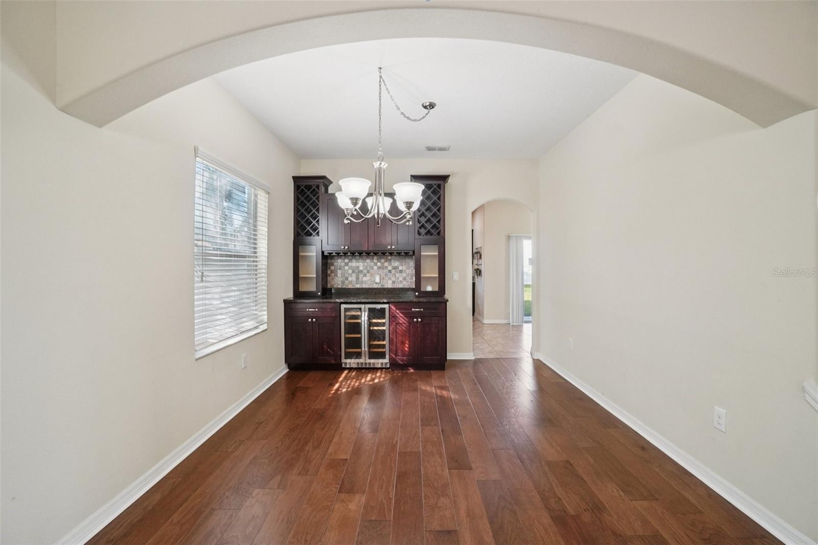 The formal dining room is highlighted by a vaulted arched ceiling detail, rich hardwood flooring, a chandelier, and a stunning built-in wet bar as the focal point, an ideal space for entertaining.