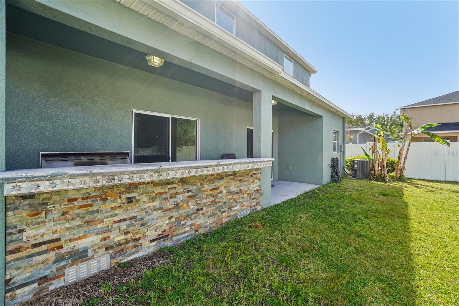 Outdoor Kitchen / Patio - This angle highlights the outdoor kitchen's stacked stone veneer base, decorative tile accent border, granite countertop, and built-in grill — all set under a covered patio overlooking the spacious backyard.