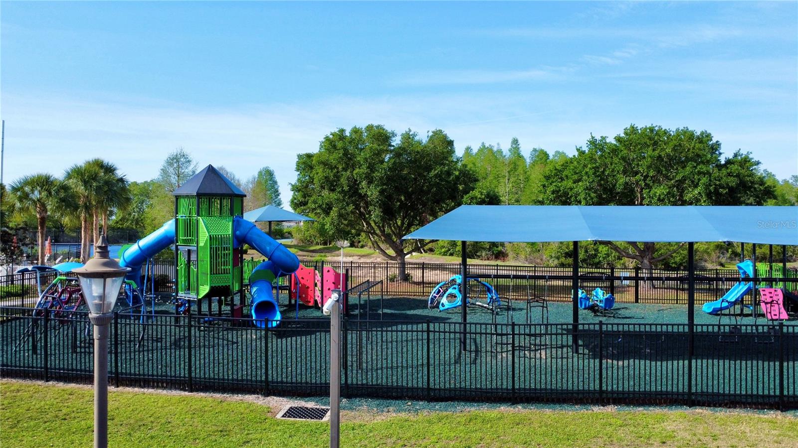 Community PlaygroundThe community playground features a large multi-level play structure with tube slides and climbing walls, a shaded toddler play area, rubberized safety surfacing, and wrought iron fencing — a well-equipped outdoor space for all ages.