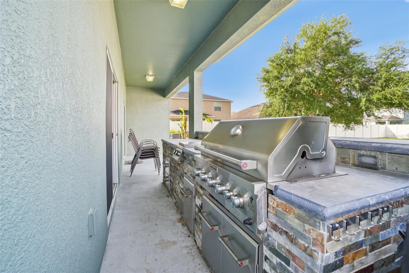 Outdoor Kitchen / Covered PatioThe covered back patio features a built-in outdoor kitchen with a stainless steel multi-burner grill, stone veneer surround, granite countertop, and overhead lighting — an entertainer's dream setup for year-round outdoor cooking.