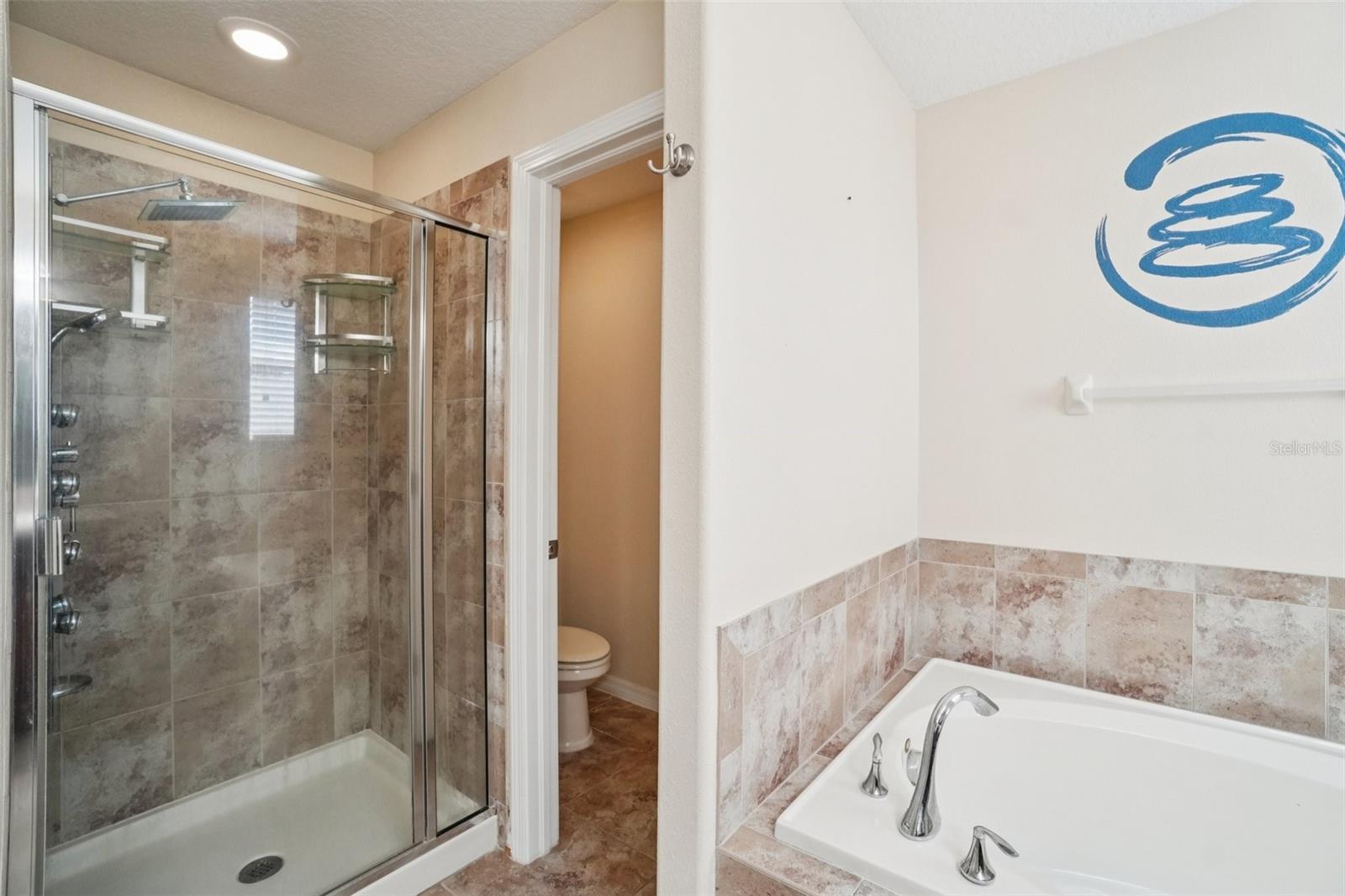 Primary bathroom with glass-enclosed shower, floor-to-ceiling tile surround, tile-surround soaking tub, and separate water closet.