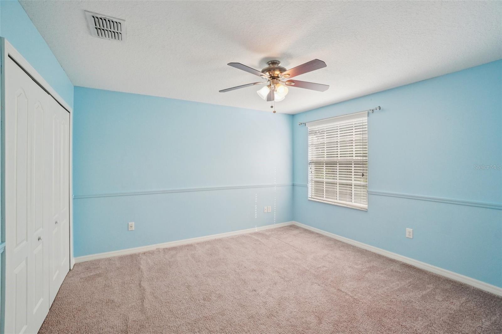 Third BedroomThis comfortable third bedroom features plush carpet, a ceiling fan, a window with natural light, a chair rail detail, and a closet — a bright and versatile space with a cheerful blue accent wall.