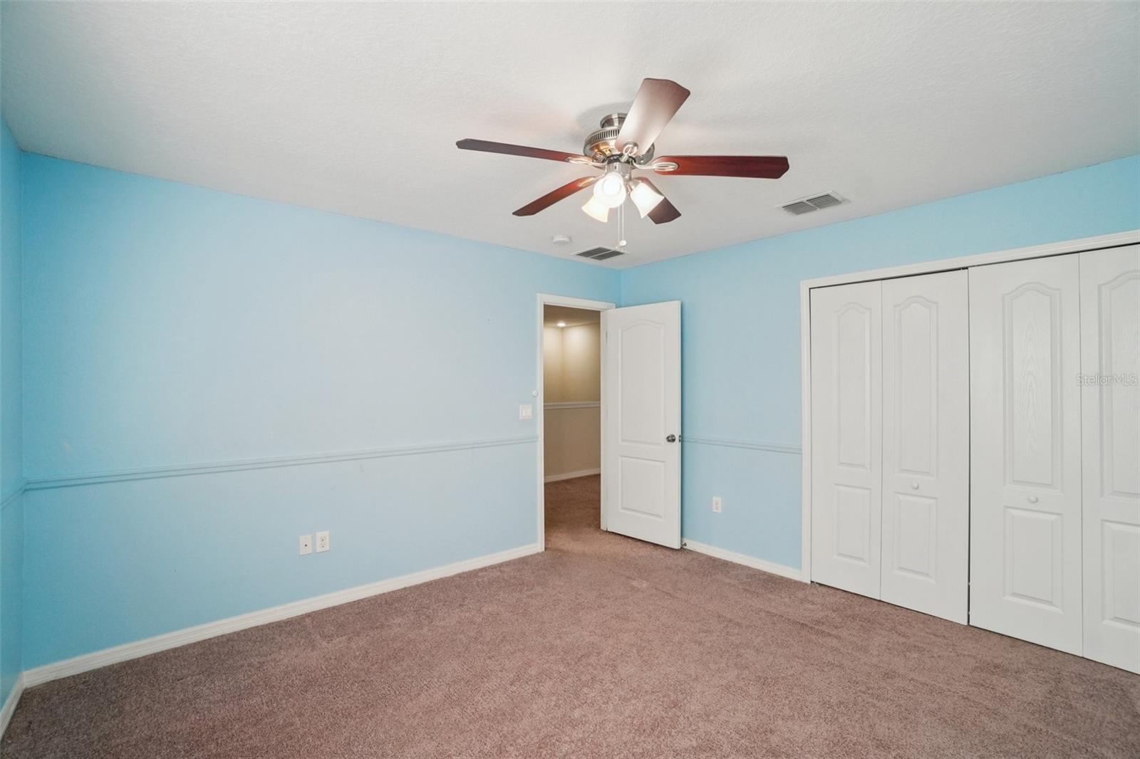 A second angle of the third bedroom shows its generous footprint, plush carpet, ceiling fan, closet, and hallway access — a well-sized room ready to serve as a bedroom, office, or flex space.