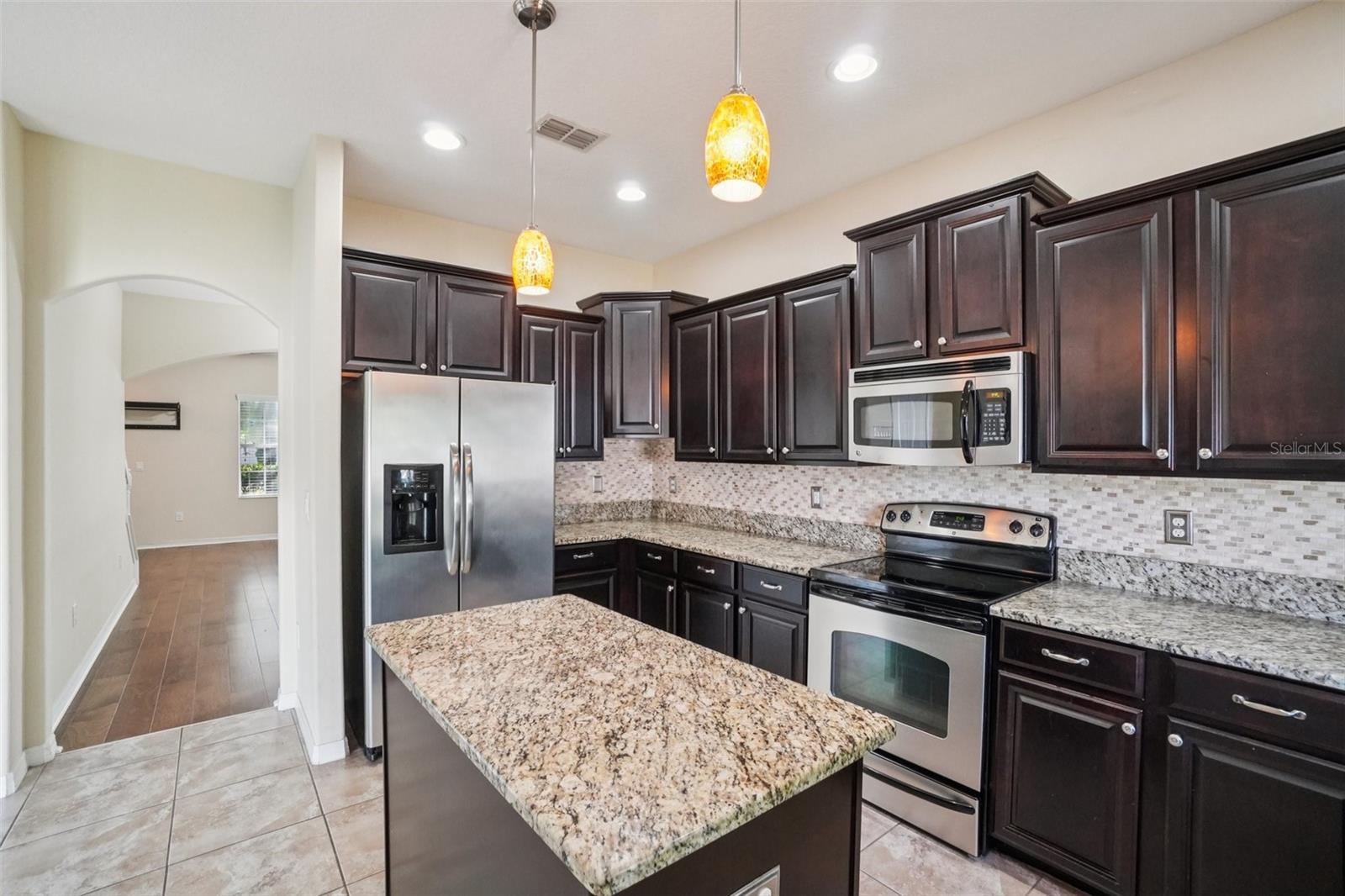 L-shaped kitchen with abundant dark espresso cabinetry, granite countertops, mosaic tile backsplash, full stainless steel appliance package including dishwasher, and window over the sink.