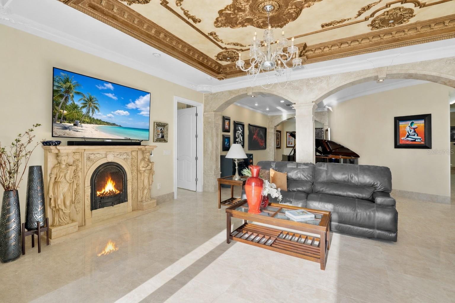 Ornate stone electric fireplace, intricate moldings on ceiling accented by chandeleirs.