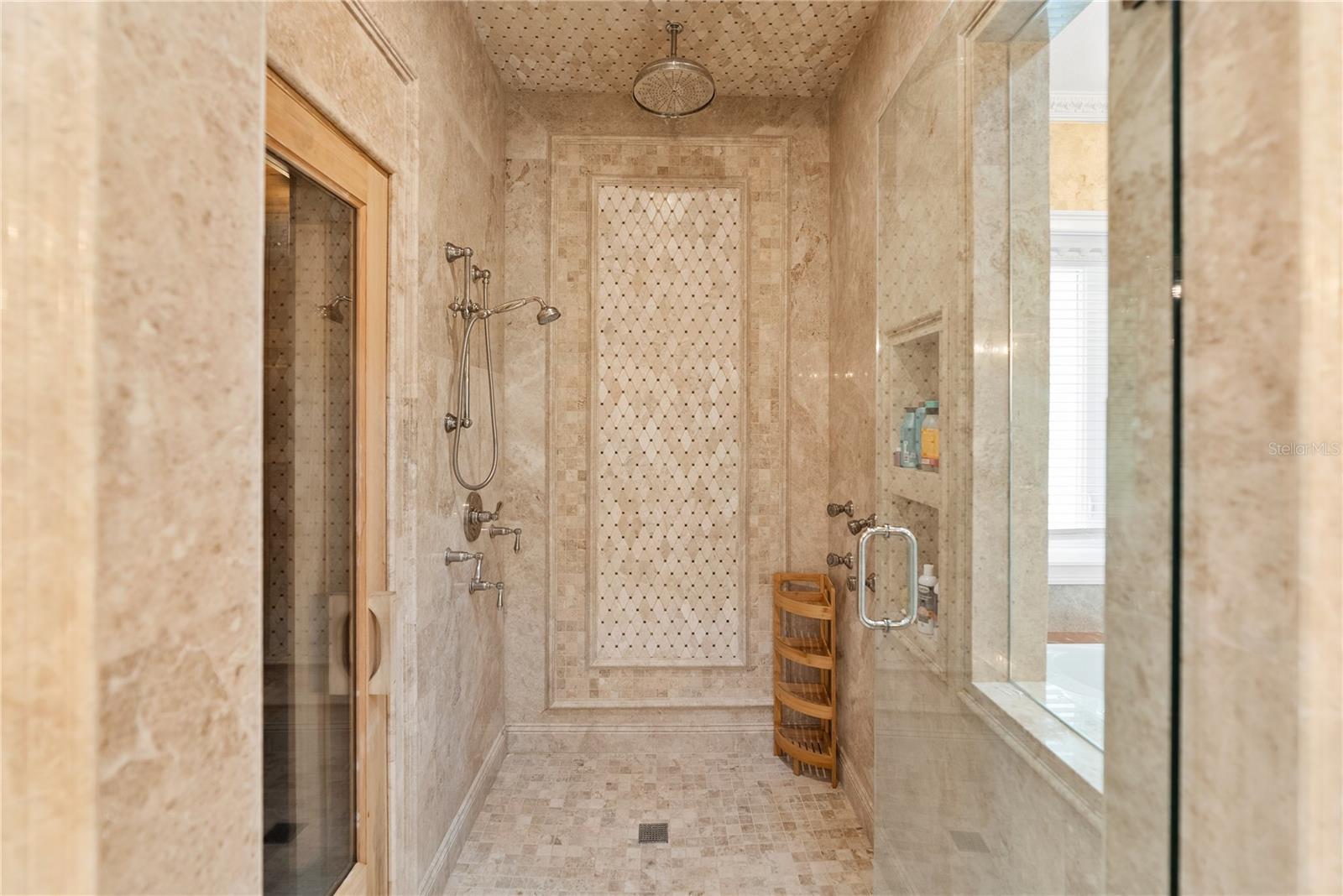 The main-level primary suite serves as a private retreat, featuring a spa-inspired marble ensuite bath with Phylrich fixtures, a large sauna, soaking tub, multi-jet full-body rain shower, multiple vanities, and expansive custom closets