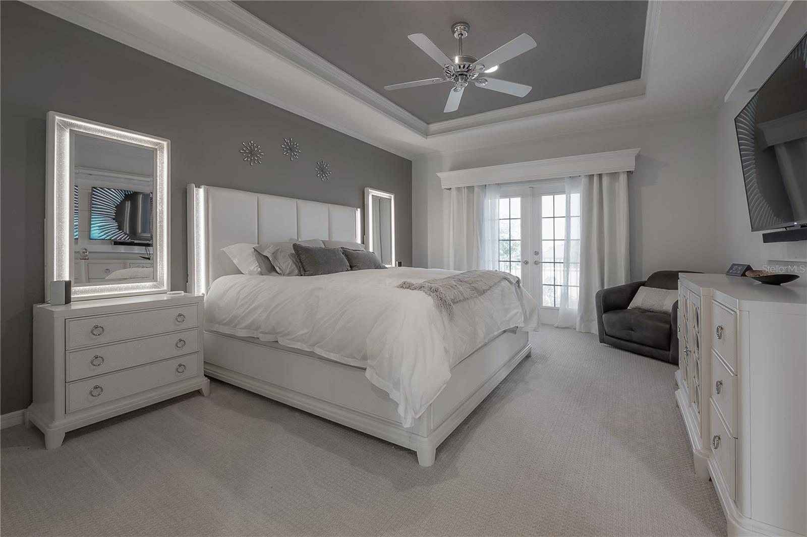 Retreat to the primary suite featuring elegant tray ceilings with crown molding, custom window treatments, and a private balcony for peaceful outdoor escapes.