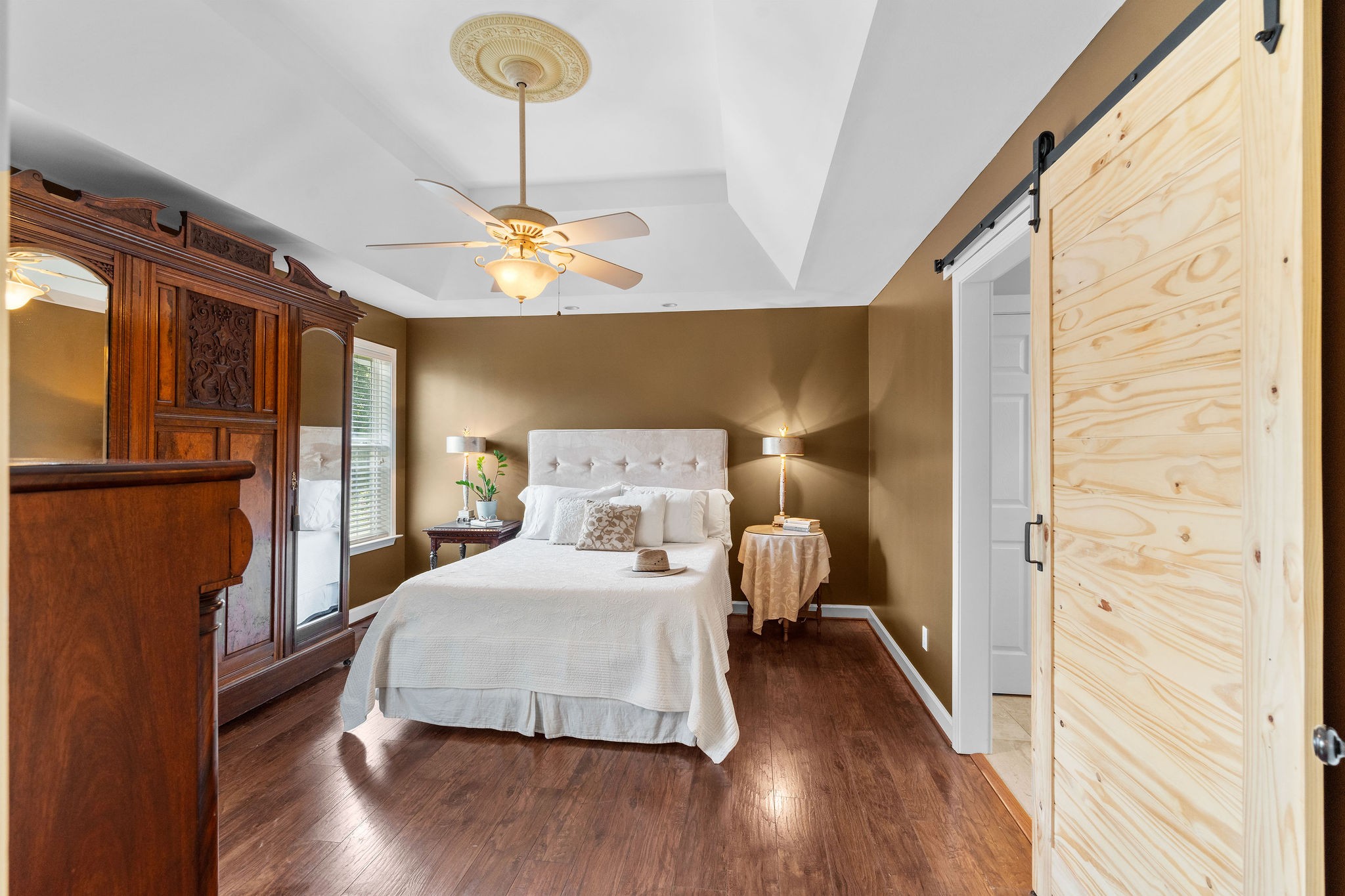 The primary bedroom is large enough to accommodate a king bed, end tables, dresser and more. It features, engineered wood flooring, tray ceiling, decorator lighting, new paint, and a floating barn door leading into the full bath.