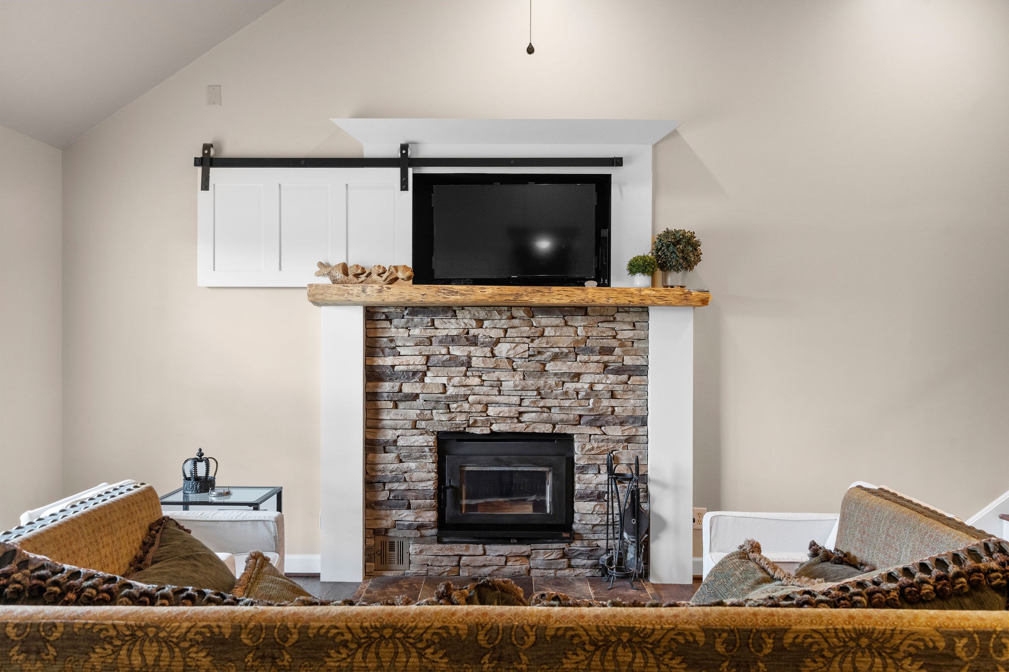 The small custom-made barn door and hardware conceals the flatscreen TV and components. The fireplace mantle is a hickory wood slab that was sourced from a Leipers Fork mill.