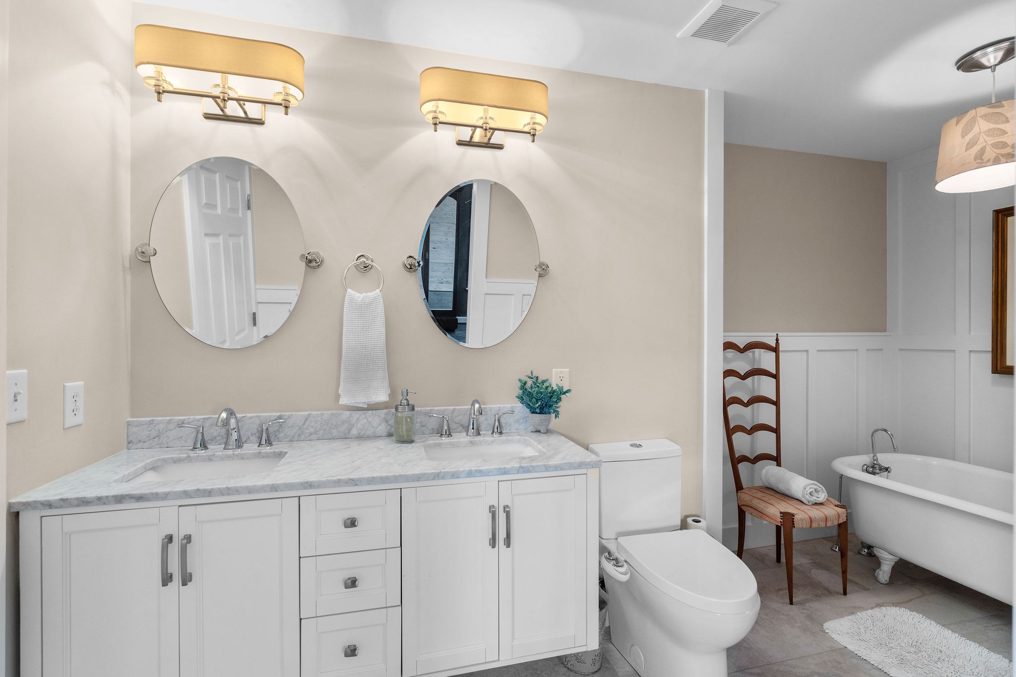 The primary bedroom’s beautiful full bath is full of vintage inspired touches — designer lighting, floating cabinets with Carrera marble countertops, ceramic tile flooring, custom board-and-batten millwork and an antique clawfoot soaking tub.