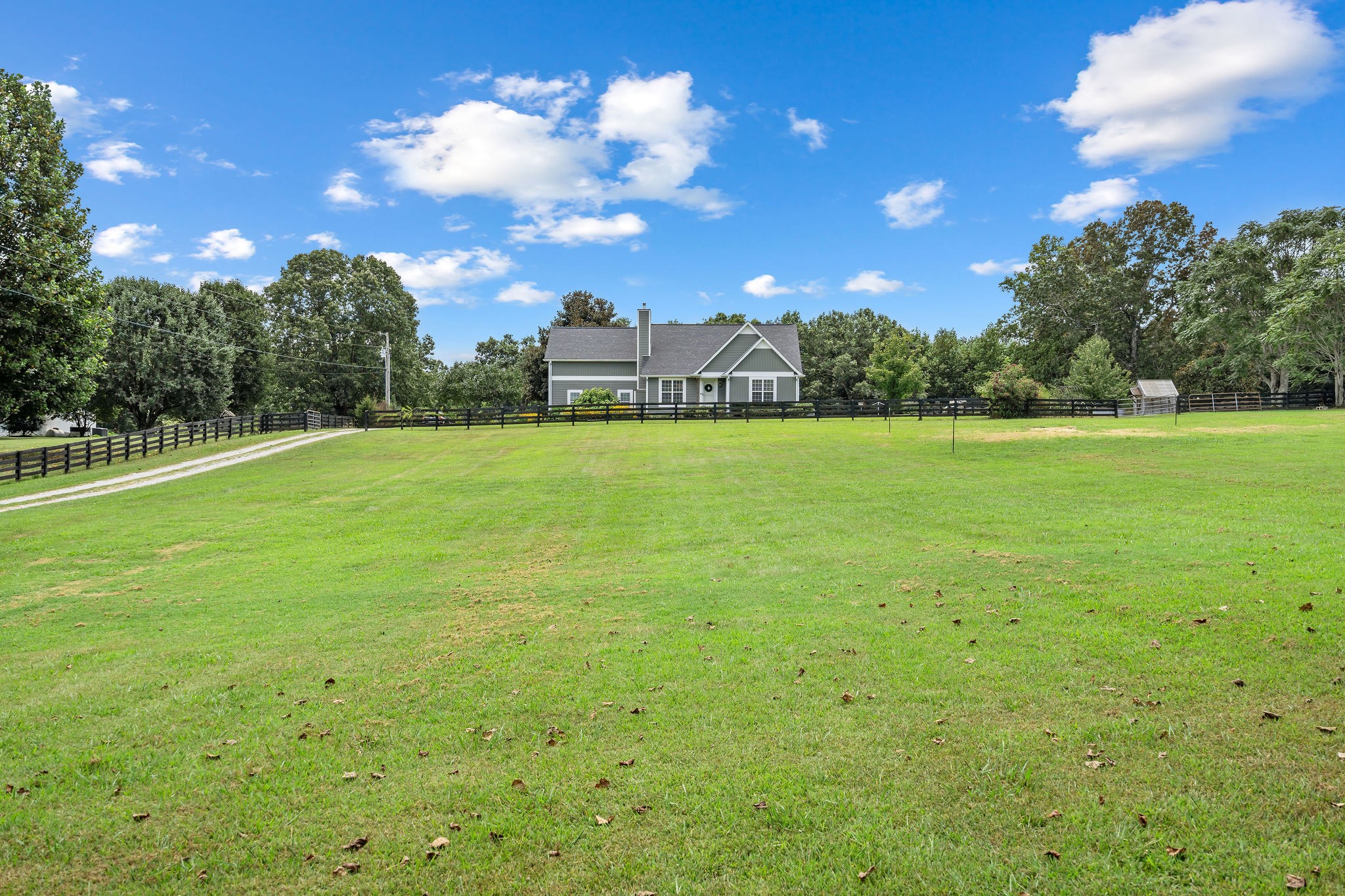The farmhouse sits back from the road. This photo shows the fence and gated front pasture. The separate gated garden area and one of the two small greenhouses can be seen to the right in this photo.