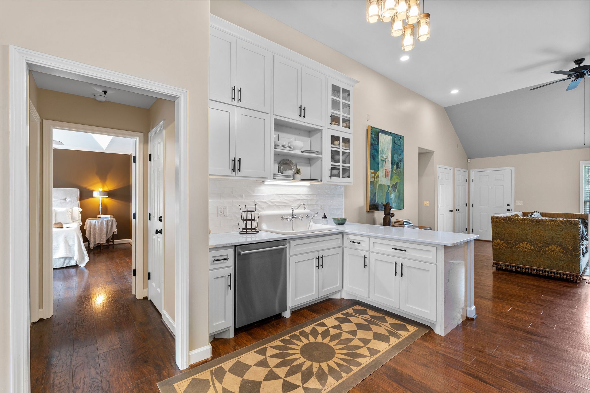 A view of one side of the kitchen, showing the custom cabinets, open shelving, display shelving, stainless steel dishwasher and high back farmhouse sink.
