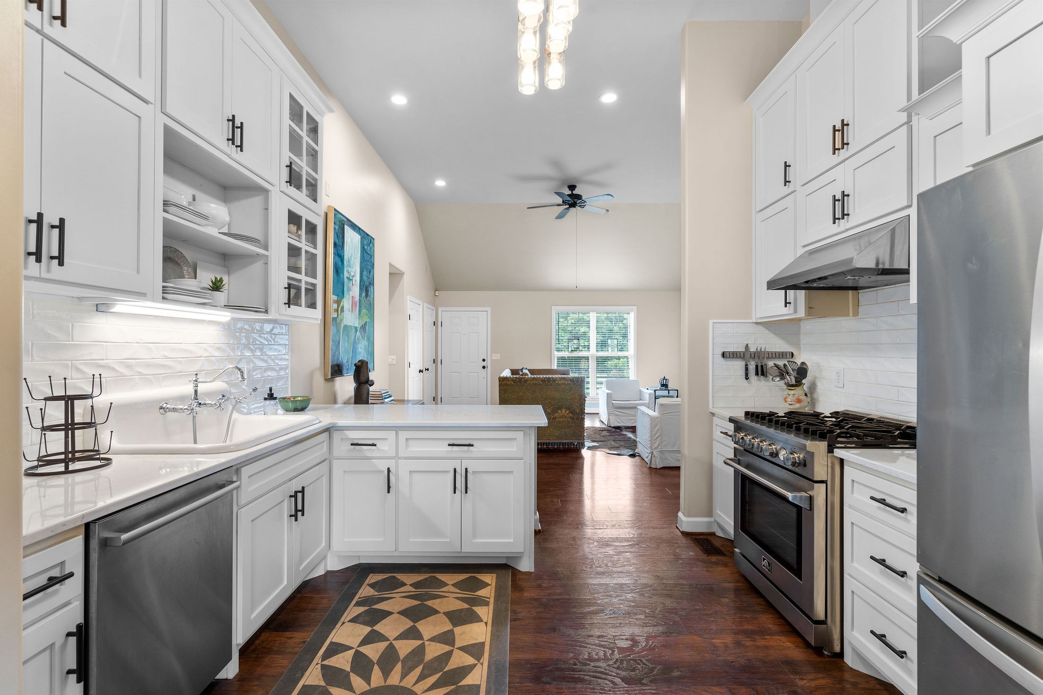 The kitchen is as functional as it is stylish, with custom Amish-made cabinets, stainless appliances, 5-burner Forno gas stove/oven, quartz countertops, tile backsplash, open shelving & glassed display area.