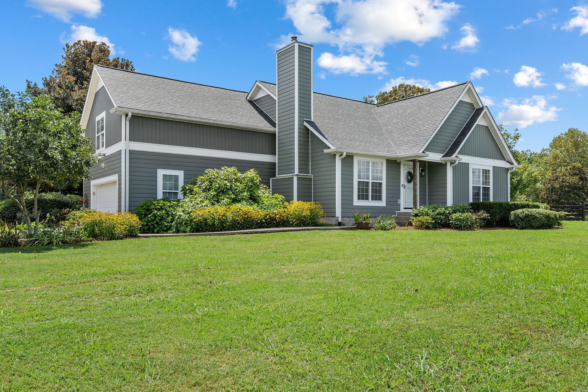 A large Oakleaf hydrangea, irises, wildflowers, Japanese magnolias, peonies, roses, azaleas, hostas, and evergreen shrubbery create a beautiful welcome for this home.