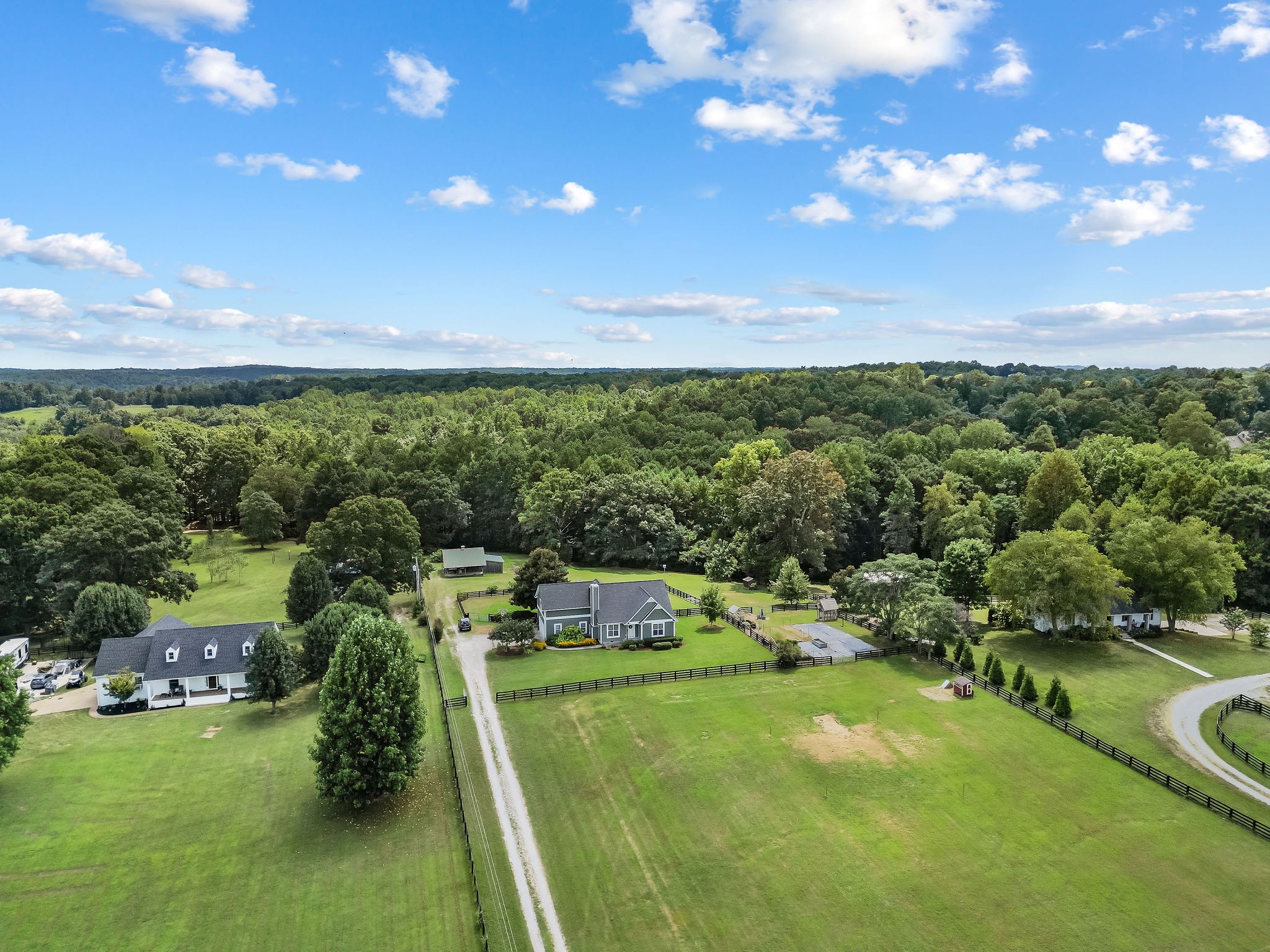 An aerial view shows the farmhouse taking center stage with fencing separating the yard from the pastures and garden area (visible to the right of the house).