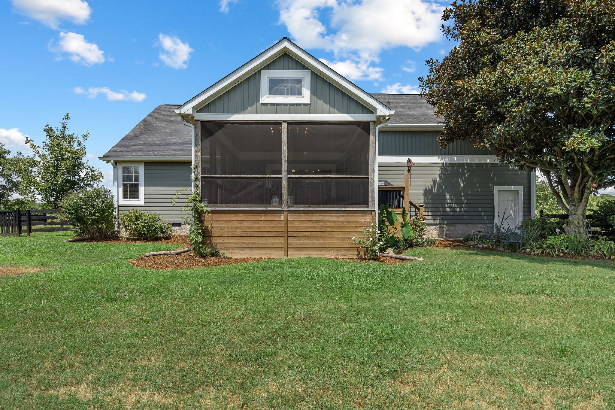 A view of the screen porch from the fenced backyard. The landscaping includes butterfly bushes, climbing roses, elephant ears, native irises, hostas, clematis, stargazer, lilies, and hydrangeas.