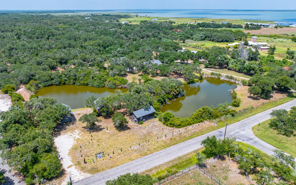 Welcome to your private retreat in the heart of Lamar! The main home features 3 bedrooms, 2.5 bathrooms, a bonus room, and a detached 2-car garage with additional storage space upstairs. Also included are three separate cabins, each with screened porches and pond views—perfect for guest stays or rental income. Set on over 7 beautiful acres with a majestic live oak forest, this unique property includes a peaceful pond surrounded by native wildlife: ducks, herons, hummingbirds, deer, and even the occasional alligator. Watch the whooping and sandhill cranes flight over your own paradise! There's plenty of land to build your future dream home while using the existing structures for income-producing opportunities. With a little sweat equity, this property offers endless potential—whether you're looking for a quiet homestead, a weekend escape, or an investment near the coast. Just blocks from Goose Island State Park, the boat ramp, and some of the best fishing bays in Texas, and only minutes to the Rockport-Fulton community! In the county, outside city limits and NO HOA!