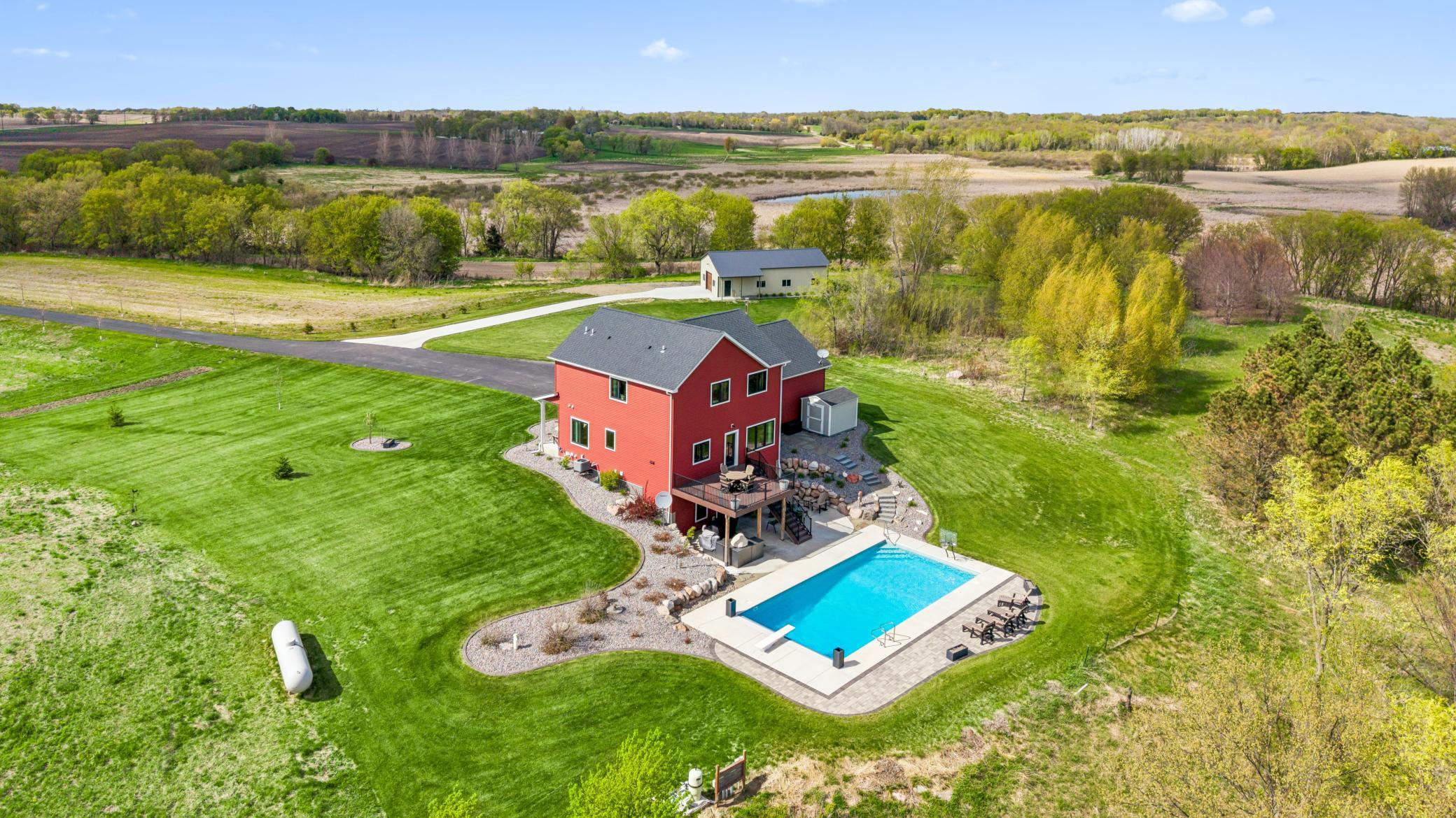 Spectacular 4-bedroom, 4-bath custom-built two-story home set on 50 breathtaking acres of woods, wetlands, and rolling hills with stunning views of Rock Lake. This exceptional property offers the perfect blend of privacy and functionality—ideal for those seeking peaceful country living without sacrificing modern convenience.  Thoughtfully designed with an open and spacious layout, the home is filled with natural light from expansive windows that showcase the surrounding landscape. High-end finishes and attention to detail are evident throughout, including custom built-ins and trim, wood-beamed accents, hardwood floors, 9-foot ceilings.  The kitchen is designed for functionality with custom cabinetry, granite countertops, slate appliances, a large center island with seating, a walk-in pantry, and both informal and formal dining spaces—perfect for everyday living and entertaining. The inviting living room with a gas fireplace flows seamlessly to a maintenance-free deck overlooking the countryside and lake views.  Upstairs offers three bedrooms on one level, featuring an oversized primary suite with a walk-in closet and private bathroom with double sinks, tile floor, soaking tub, and tile shower, as well as an additional full bath and convenient laundry room.  The walkout lower level provides additional living space with a large family room with built in bookcases and a free-standing wood stove, fourth bedroom, full bath, and a relaxing sauna.  For outdoor living, the home features a maintenance-free 16x18 deck and an oversized concrete and paver patio leading to a 20x40 heated inground pool with an automatic cover.  The expansive acreage offers endless possibilities for trails, recreation, hunting, gardening, or raising animals.  Car enthusiasts and hobbyists will appreciate the heated 4-car attached garage that includes a climate-controlled 14x35 bonus room above, and an impressive 30x50 detached garage with concrete floor and drive—ideal for additional vehicles, boats, RVs, or workshop space.  With a 26kW Generac backup generator and an irrigation system already in place, this well-maintained estate offers a quiet country lifestyle just minutes from Hwy 55, local trails, and shopping.  This extraordinary estate offers peaceful country living, spectacular views, and unmatched versatility. A rare opportunity to own a true legacy property.  Welcome home.