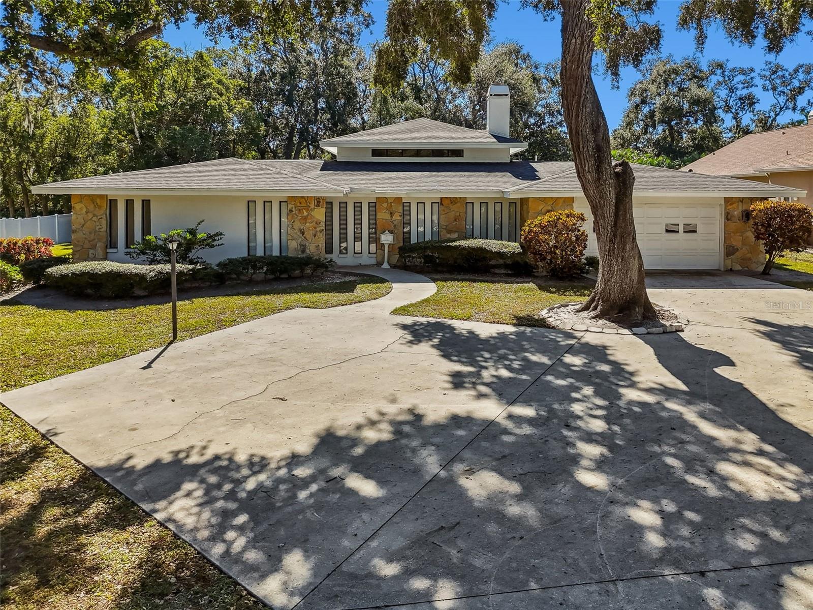 Set on an impressive .68 acre lot in a quiet Clearwater neighborhood near beautiful Safety?Harbor, this spacious four bedroom, three and a half bath pool home offers room to grow, refresh and make your own. Surrounded by mature trees and an expansive front and backyard, the property welcomes you with a timeless single level elevation and a large driveway leading to a two car garage.Inside, you’re greeted by a foyer that introduces a thoughtful split floor plan. One wing houses a private primary suite with its own en suite bath, while the opposite side of the home features a second suite plus two additional bedrooms and baths, perfect for multigenerational living or guests. The heart of the home is an inviting family room with a stone fireplace and custom built ins, opening to a formal dining area and a kitchen with abundant cabinetry, stainless appliances and a pass through window to the lanai.Sliding doors lead to an expansive lanai with plenty of covered space for outdoor dining and lounging. An in ground screened pool with a stone waterfall feature anchors the backyard, and there is still ample lawn for play thanks to the home’s generous fenced in lot. This spacious lot had endless possibilities. Upgrades including a new roof (2022), solar panel system (2023), HVAC (2022) make this property both comfortable and energy efficient, while no HOA and a Flood Zone X designation add peace of mind.Moments from Safety?Harbor’s waterfront park, downtown eateries and Gulf beaches, this well cared for home provides a rare combination of land, privacy and potential. Bring your vision and make it your own!