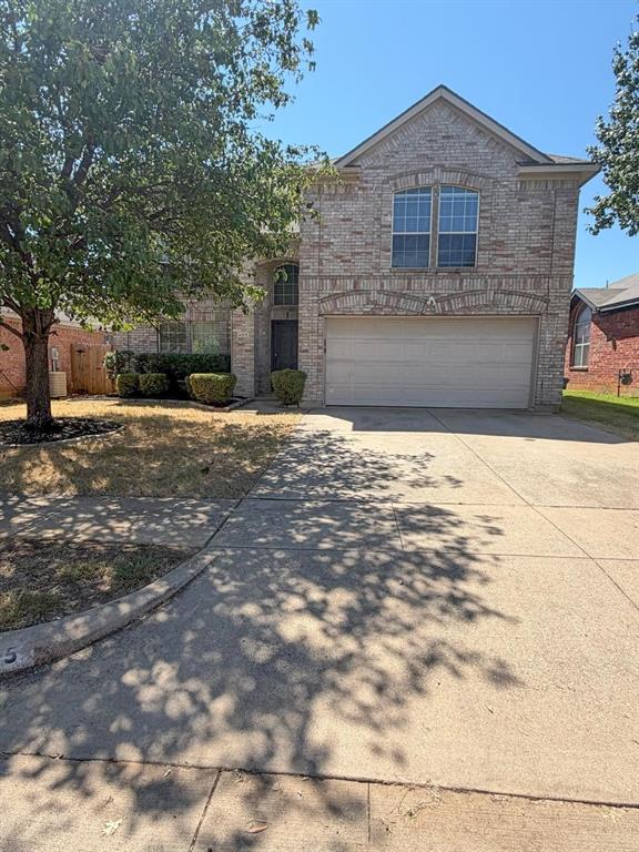 Brick facade with arched window accents, attached two-car garage, and mature front yard trees