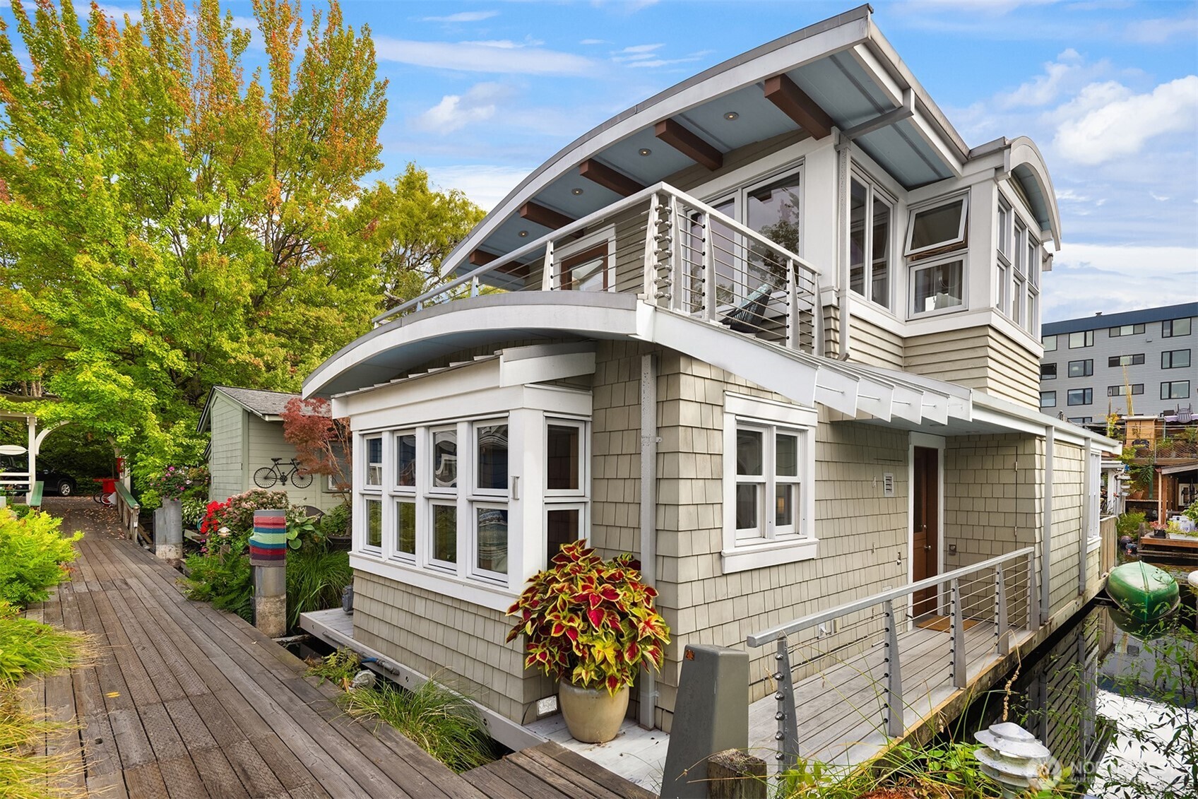 A cheerful white pergola welcomes you onto the dock at Tenas Chuck Moorage — a neighborhood unlike any other. This sunny south-facing floating home was re-imagined in 2004, and rebuilt to embrace history while elevating modern dockside living. A sprung roof over cedar shake siding, a rooftop deck with cable railings, a chambered concrete float — from the dock, a timeless silhouette that belongs on the water. Inside a NanaWall accordion glass door opens the great room entirely to the waterside deck, dissolving interior and exterior lines. Two back-to-back fireplaces (gas or wood) serve both interior and deck. The outdoor masonry fireplace doubles as a grill, adding activity and joy to every season. The kitchen is built for cooking & entertaining: DCS range, Subzero refrigerator, Fisher & Paykel dish drawers. Anigre-paneled walls with custom art hangers, cove lighting, heated floors, and whole-house audio wiring give the interior a warm, modern, considered feel. Custom-tiled jetted tub and extensive built-in storage throughout. Includes small boat & paddleboard moorage on 3 sides. Eastlake's Tenas Chuck Moorage is a registered historic floating home community with nearby parking and EV charging available. Steps from Eastlake's Smallest Floating Home Museum, shops, groceries, and restaurants. And when the Fourth of July arrives, you already have the best seat in Seattle. Come join us on the lake!