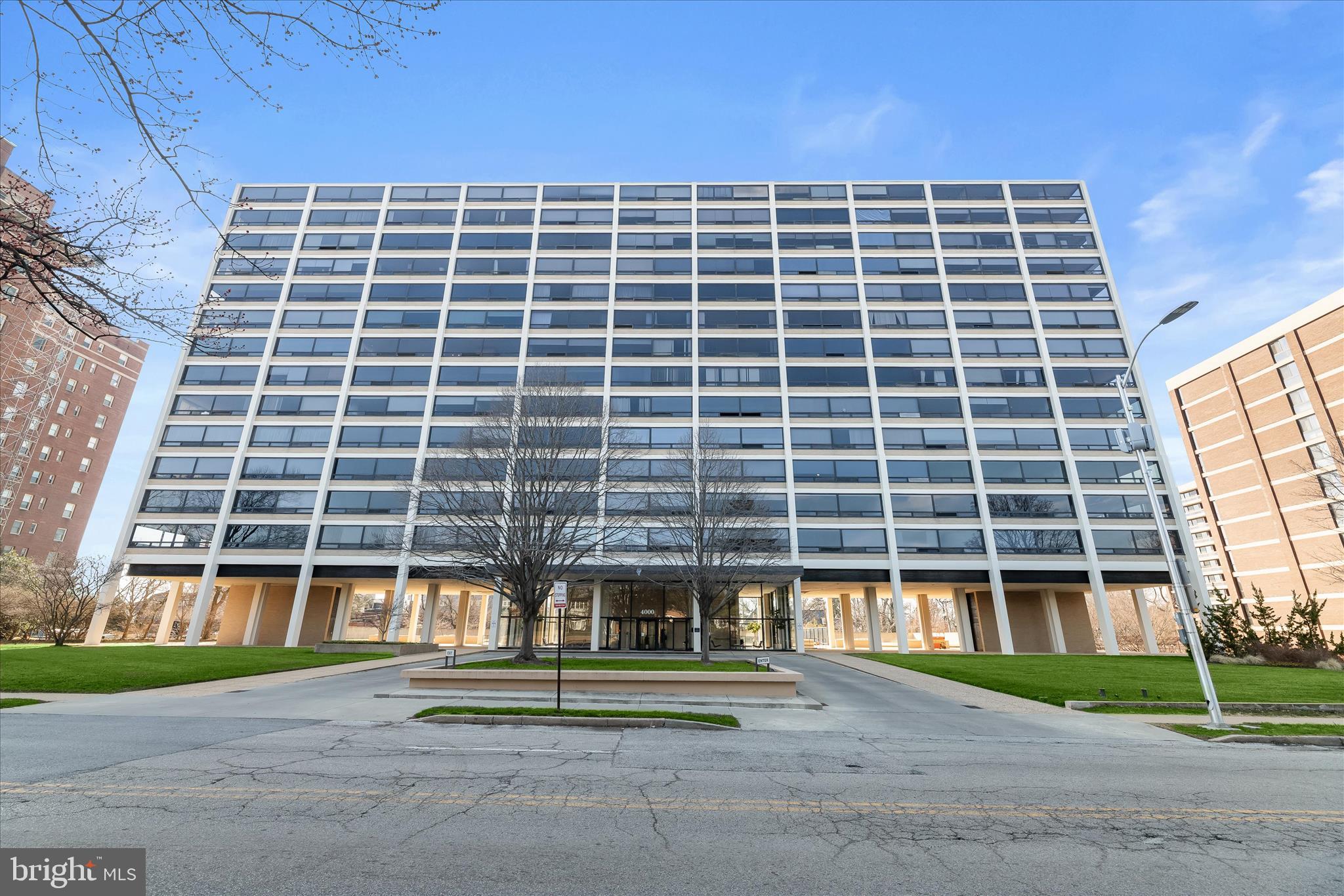 Mid-Century Modern style meets panoramic views in this expanded, move-in ready executive-inspired residence. Originally designed as a unit with two smaller bedrooms, the home has been thoughtfully reimagined to create a spacious one-bedroom, one-and-a-half-bath condo with an open and airy living environment. Located on a tree-lined street in the charming Tuscany-Canterbury neighborhood, the building welcomes residents with a staffed lobby and elevator access to this light-filled home. Its prime location places you just moments from the Homewood campuses of Johns Hopkins University and Loyola University Maryland, offering convenience for academics, medical professionals, and anyone who appreciates easy access to these vibrant institutions.  This is your opportunity to live in a rare corner unit condo in Historic Mies van der Rohe-designed Highlfield House. Inside, clean architectural lines and an open concept layout create a sophisticated yet comfortable setting. A dramatic wall of floor-to-ceiling windows fills the living space with natural light while framing sweeping views of the surrounding tree-lined neighborhood. The generous footprint offers exceptional flexibility, allowing you to arrange the living and dining areas in a way that suits your lifestyle and creativity.The galley kitchen offers a functional layout with easy-care ceramic tile flooring, contemporary lighting, open shelving, a stylish backsplash, a gas range, and ample countertop space for everyday meal preparation.The spacious primary suite is thoughtfully designed to balance comfort, storage, and versatility. Custom light wood cabinetry spans the length of the room and serves as a striking focal point while providing generous dresser storage and built-in shelving. This integrated design transitions into a wide, illuminated work surface that can function as a home office desk, vanity, or creative workspace. The suite continues into a private wing that includes a large walk-in closet with built-in organization and a private en suite bath, creating a quiet retreat at the end of the day. Rich hardwood flooring and a clean, neutral palette continue throughout the suite, reinforcing the home's cohesive design and airy feel.Residents also enjoy a variety of building amenities, including 24-hour on-site security, valet services, and access to a beautiful community pool that provides a relaxing outdoor retreat during the warmer months.Note:  Select interior photos have been virtually staged.