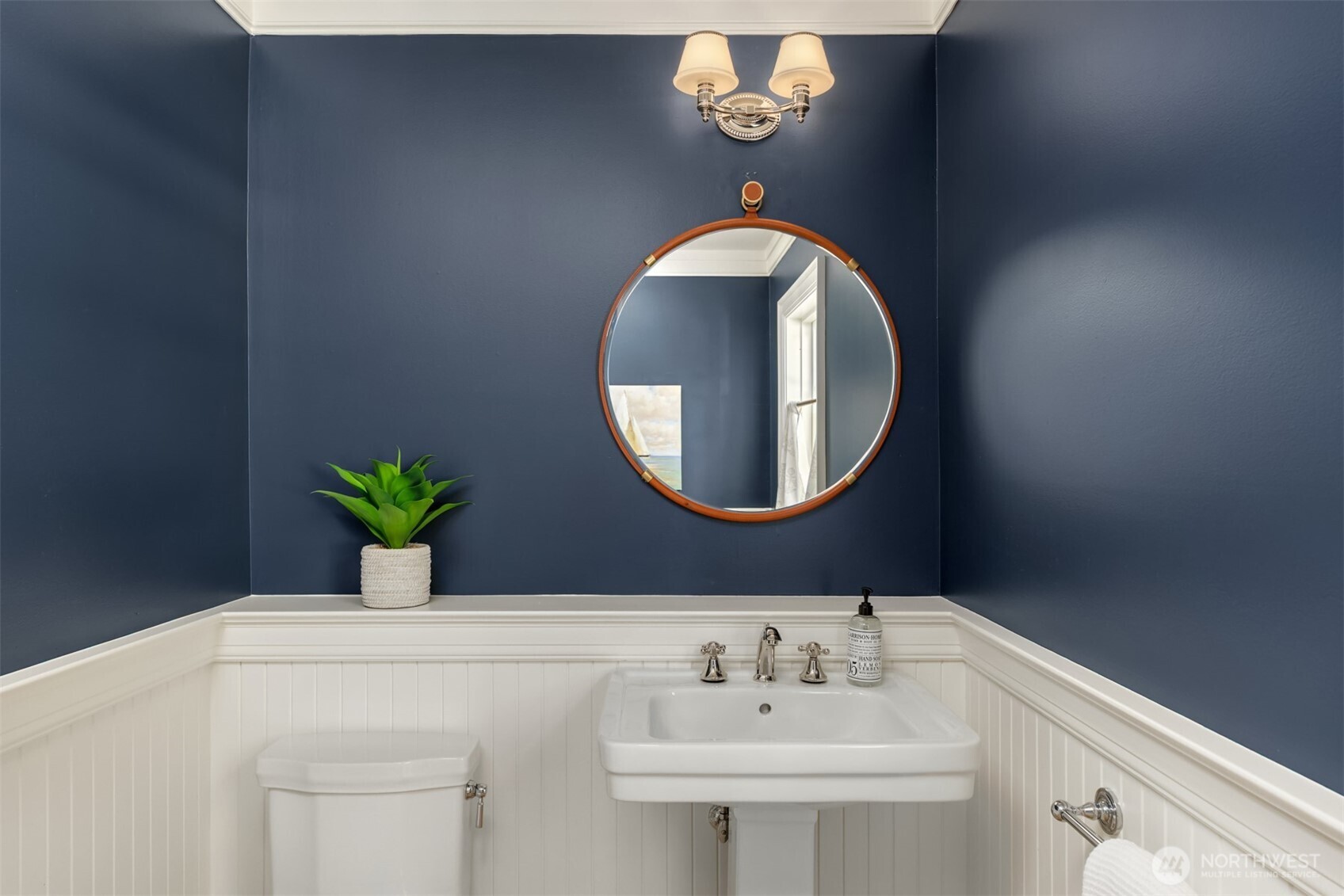 Stylish powder room featuring a pedestal sink and a round mirror.
