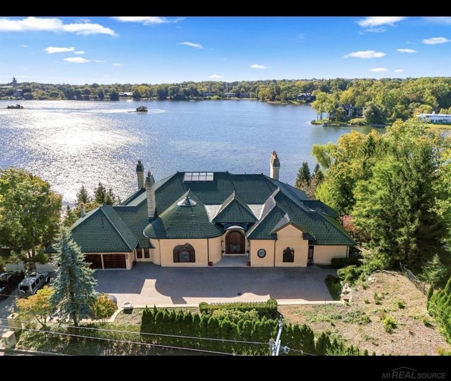 Set along the shores of Island Lake in the prestigious community of Kirk in the Hills, this custom-built lakefront estate offers over 14,000 square feet of architectural presence, privacy, and craftsmanship that would be nearly impossible to replicate today. Designed and built with extraordinary attention to detail, this is truly a one-of-a-kind residence. From the moment you enter, soaring 18-foot ceilings, expansive lake views, and natural light create a feeling that is both grand and calming - more like arriving at a private resort than coming home. This property is not designed for everyone. It was created for those who value originality, craftsmanship, and spaces that feel like a permanent vacation. Imagine waking each morning to breathtaking sunrises over the water, with panoramic lake views visible from multiple main living areas and bedroom suites. The home features four private bedroom suites, including a primary retreat with fireplace, terrace access, dual dressing rooms, spa-style bath, and oversized walk-in closets. With over five bathrooms and multiple entertaining spaces, the home balances large-scale gatherings with quiet, private living. The gourmet kitchen is finished with top-tier appliances including Sub-Zero refrigeration, a Viking range, custom SieMatic cabinetry, and radiant-heated flooring, opening seamlessly into gathering and dining spaces overlooking the lake. A mahogany library with coffered ceilings and built-in shelving adds warmth and character, while a hidden passage connecting the living room and office reflects the level of custom design carried throughout the home. The finished lower level is designed for entertaining and extended living, featuring a second kitchen, imported Italian bar, wine cellar, recreation and game spaces, sunroom, daylight bedrooms (including walkout access), and dedicated lakeside storage with lower-level garage access.