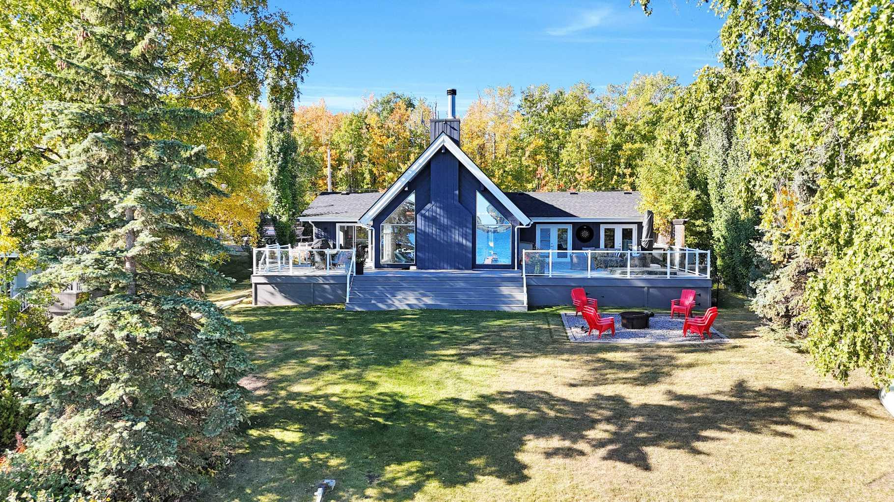 Looking for a true five bedroom lakefront bungalow in Norglenwold with meaningful upgrades? It exists. Welcome to 187 Grand Avenue. This home offers 2,300 square feet of pristine Sylvan Lake living, featuring a fully renovated main level, 75 feet of level waterfront, and unobstructed lake views. Inside, painted cedar vaulted ceilings, a full height stone fireplace, and floor to ceiling windows set the tone. The open concept main level has been completely transformed with a redesigned kitchen, new appliances, new flooring, trim, baseboards, doors, windows, lighting, and fresh finishes throughout. Outside, the oversized lakeside deck is built on screw piles with composite decking, dual gas lines for a BBQ and fire table, a sunken hot tub area, and easy access down to the retaining wall and the lake. The fully fenced front yard is ideal for kids or pets, while the heated 25 by 23 garage handles toys, tools, and lake gear with ease. The basement is protected by three sump pumps, each with battery backup and alarm systems. Two air conditioners and new furnaces installed in 2024 provide efficient year round comfort. Skate in the winter, boat in the summer, and enjoy everything in between. This is four season lake living, done right.