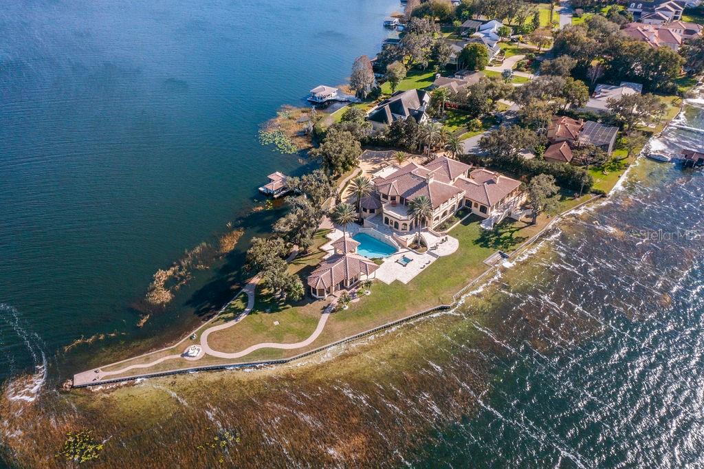 Nestled along almost 1,000’ of the highly sought after Butler Chain of Lakes in Windermere, this exquisite Mediterranean estate beckons with unrivaled opulence. Beyond a private gate, a 2-acre peninsula reveals a masterpiece of architectural brilliance designed by Nasrallah and built by Ray Coudriet. The grand entry sets the tone, with a majestic staircase, a 25+ft hand-painted rotunda ceiling, and a stunning 10-ft Waterford chandelier. Every inch of this residence exudes sophistication, from the marble floors and corbels to the intricately carved fireplace mantels or even the ornate door hinges. Boasting 5 spacious bedroom suites, four with outdoor walk-outs, in the main home, complemented by a separate guest/staff apartment, this estate offers flexibility and privacy. A resort-style pool, cabana, along with a boathouse, dock and paver paths meandering through the property, create an outdoor haven for entertaining and relaxation. The guest quarters or a private office that takes in views from 3 sides. Architectural marvels abound, with handcrafted coffered ceilings, exposed wood beams, and a gourmet kitchen featuring a red brick barreled ceiling and appliances by Wolf and Sub-Zero. Hosting events is effortless with a separate full caterer's kitchen. The primary suite offers serene panoramic water views, complemented by an extraordinary dressing room and bathroom. For wine connoisseurs, a climate-controlled 3,000+ bottle wine cellar awaits. Verandas and terraces afford fresco dining, bar area and sweeping views, enhancing the outdoor experience. Work in the masterful office with birds’ eye 180-degree water views or step into the game room for a game of pool or a sunset view off the balcony. A large travertine parking area for events and a 4-car garage adds practicality to this extraordinary property. This masterpiece transcends the ordinary, offering a lifestyle of unparalleled luxury and sophistication. Seize the opportunity to make this stunning estate your own.
