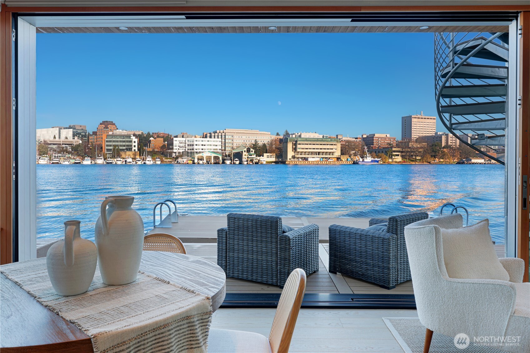 Newly constructed and expertly built by Lithic Construction, this floating home embodies quiet sophistication from its premier end-of-dock setting on Portage Bay. A warm modern aesthetic highlights sweeping 180-degree views and seamless indoor–outdoor living through a 20-foot, floor-to-ceiling sliding door system. Auto shades for complete privacy. Natural cedar siding is paired with custom steel railings and a striking staircase. The primary suite features 14’ vaulted ceilings and an ensuite bath. A rooftop deck, front patio, and auxiliary raft provide approximately 950 sqft of outdoor living. Includes rare 28’ separately deeded boat moorage + two parking spaces. Experience the best of the Pacific Northwest living in a waterfront sanctuary.