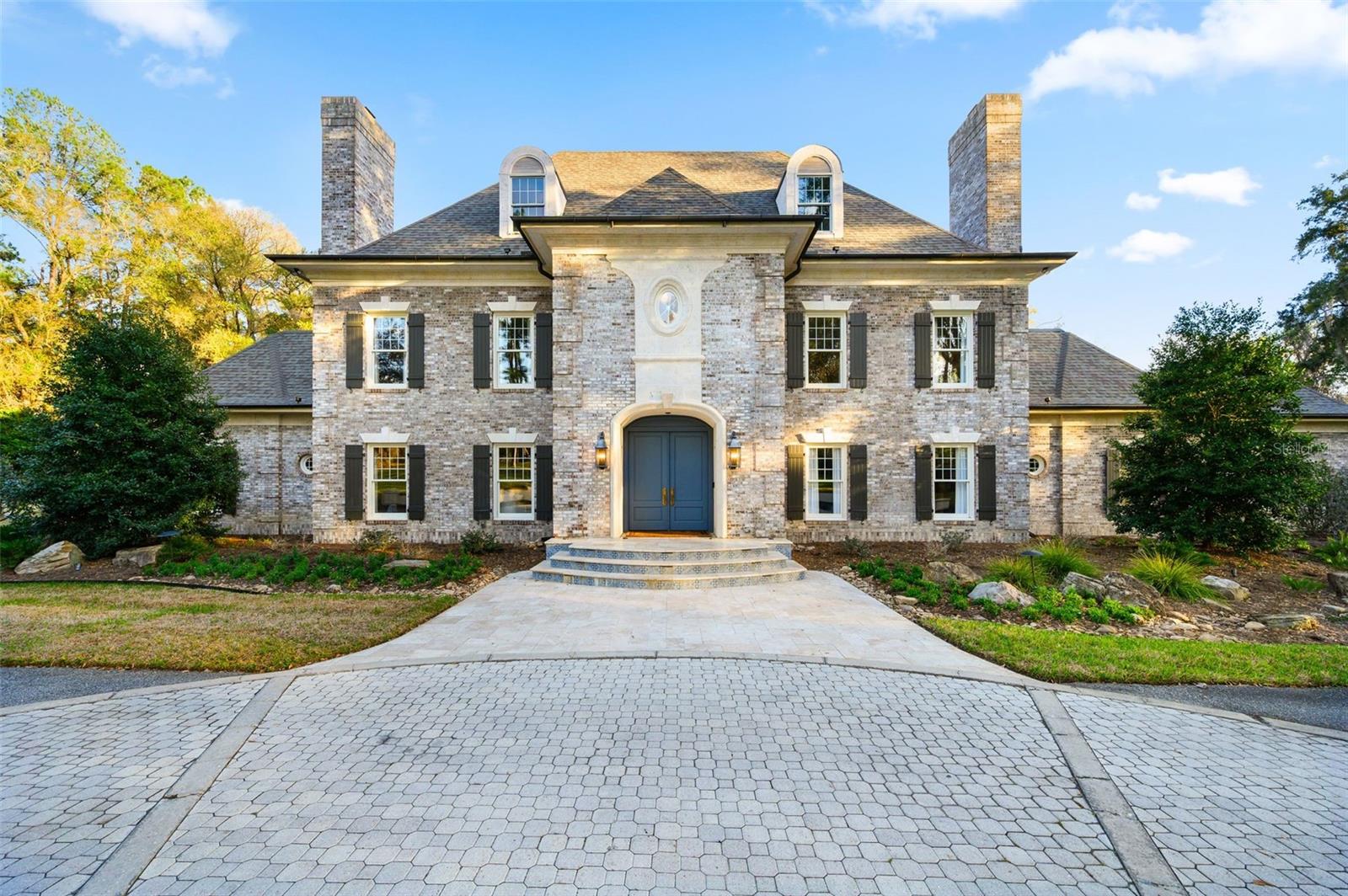 Set on 6.81 secluded acres in the exclusive Tomoka Hills enclave, this extraordinary French Provincial estate offers a rare blend of privacy, elegance, and resort-style living. Exceptionally designed and spanning nearly 6,000 square feet in the main home and over 2000sf in the new guest house, the residence showcases a thoughtfully designed floor plan that flows effortlessly for both comfortable daily living and sophisticated entertaining.Remodeled by local custom builders, the home features impeccable craftsmanship and high-end custom details throughout, reflecting remarkable attention to fit and finish. The main residence includes four spacious bedroom suites, all en suite, along with 5.5 bathrooms.Inside, gorgeous hardwood floors unify the entire home while a dramatic two-story foyer with intricate woodwork welcomes guests and frames immediate views through French doors to the pool and completely private backyard. The first floor offers multiple gathering spaces, including a sitting room with fireplace, formal dining room that flows through a Butler's Pantry to the kitchen and a spacious family room with a nearby half bath and wine bar—ideal for entertaining.The luxurious primary wing serves as a private retreat, featuring a sitting room (or office), a spa-inspired bath with a free standing tub, separate marble vanities, and a large walk-in shower finished in Calacatta marble with rain shower head and multiple shower heads. A large dressing room with an extensive organizational closet system completes the suite.Designed with entertaining in mind, the formal dining room connects to the stunning chef’s kitchen through a separate butler’s pantry, providing the perfect space for catering prep and seamless hosting. Upstairs, a gracious landing with open-air balcony access leads to three additional private suites, plus a flexible bonus room with built ins.Adding tremendous value and versatility to the property is a newly constructed 2,100-square-foot detached guest house. This luxurious residence offers two bedrooms (one BR is currently used as a GYM with rubber mat flooring), one bathroom, a spacious living room, and a full high-end designer kitchen with premium finishes. Perfect for guests or extended stays, the guest house also features a large summer kitchen with motorized screens, creating a seamless indoor-outdoor living experience that flows beautifully to the resort-style pool area. With its designer finishes, spacious layout, and luxurious feel, this guest residence functions as a private retreat within the estate.This remarkable property combines refined European-inspired architecture, modern luxury updates, and expansive grounds, creating a truly exceptional estate setting located in a prime location in SW Gainesville.