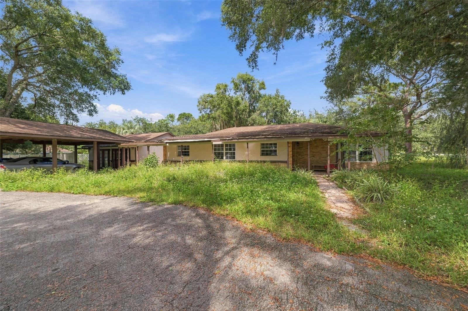 Set on a massive 1-acre corner lot, this fixer property offers 4 bedrooms, 4 bathrooms, a detached guest house, carport, and plenty of space to bring your vision to life. The covered front entry, accented by brick columns and brick detailing, creates a welcoming first impression. Step inside to the foyer, where tile flooring and a paneled ceiling continue toward the dining area. The dining room features wood flooring and an open connection between the entry, kitchen, and additional living space, creating a natural flow through the main areas. To the right, the kitchen offers crown molding along the ceiling, extensive wood cabinetry with upper and lower storage, a dual sink with an interior pass-through window above, and a pantry for added convenience. Just beside the kitchen, the living room provides a spacious layout with vinyl flooring and multiple large windows that bring in natural light. To the left of the dining area, an additional room features matching tile flooring, multiple windows overlooking the surrounding property, and a door leading toward the detached guest area. The generously sized primary bedroom continues with vinyl flooring and includes a built-in closet and private en-suite bathroom. The en-suite features a single vanity with white cabinetry and a glass-enclosed tub/shower combination surrounded by tile. Bedrooms 2 and 3 offer similar layouts, with each featuring its own private bathroom and built-in closet. Bedroom 2 also includes sliding glass doors leading to the covered patio. Both private bathrooms feature single vanities, with one offering a glass-enclosed tiled tub/shower combination and the other a glass-enclosed tiled shower. From the additional room, a pass-through door leads toward the detached guest area, with a paved patio providing a transition between the main home and guest house. The detached guest house offers light-toned tile flooring, its own dining area, and a kitchen with white cabinetry, ample countertop space, wall-mounted shelving, and a window above the sink. A private bathroom includes a single vanity with wood cabinetry for storage. Step outside to discover a spacious patio finished with patterned tile and an in-ground pool that is currently not in use, offering an opportunity to restore and reimagine the outdoor space. The entire backyard is enclosed by a white vinyl privacy fence, while mature trees around the perimeter create a natural backdrop and added privacy. Located in the Brooksville area, the property is near Withlacoochee State Forest, offering hiking, fishing, wildlife viewing, and outdoor recreation, while Weeki Wachee Springs State Park provides spring-fed waters, kayaking, swimming, and its famous mermaid shows. Nearby parks, shopping, dining, and other Brooksville-area amenities add convenience to the location. With its oversized corner lot, multiple bedrooms and bathrooms, detached guest house, pool, carport, and flexible living spaces, this property offers a substantial opportunity for renovation and customization.