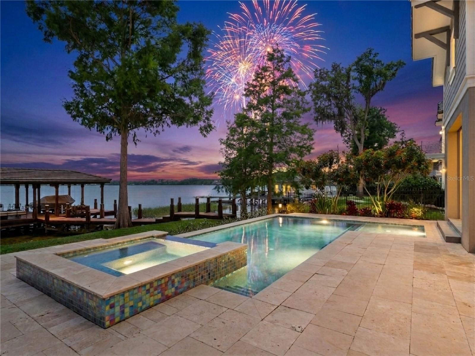 One or more photo(s) has been virtually staged. A Custom Estate on one of the Butler Chain's most coveted stretches of shoreline. Situated near the tip of a peninsula lot, the home captures panoramic water views of Lake Tibet, Lake Sheen, and the connecting canal from nearly every room. The south-facing rear orientation delivers sunrises over the water each morning, golden sunsets each evening, and nightly Disney World and EPCOT fireworks reflected across the lake after dark. The Disney Springs hot air balloon is visible from the yard. Step from the back of the home directly to your private dock and boat lift on Lake Sheen — one of Florida's premier ski lakes — in seconds. Whether you're loading ski equipment, tubes, fishing tackle, or a cooler, the water is right there. The Butler Chain offers over 4,700 acres across 11 interconnected lakes, renowned for world-class water skiing, wakeboarding, tubing, and trophy largemouth bass fishing. Inside, the open-concept floor plan was designed for effortless entertaining. The chef's kitchen features premium appliances and flows seamlessly into the main living area, where walls of sliding glass open to the resort-style pool, spa, summer kitchen, and fire pit — all framed by unobstructed water views. A glass-walled wine room, butler's pantry, and formal dining area set the tone for refined living. The main-floor primary suite is a true retreat, with vaulted ceilings, a wall of windows facing the lake, and a spa bath featuring a soaking tub overlooking the water. Five bedrooms, five baths, and dual laundry rooms — one on each floor — complete the interior. A three-car garage finishes the package. Situated in FEMA Flood Zone X, no flood insurance is required — giving you all the beauty of waterfront living on the Butler Chain without the added cost that accompanies most lakefront properties in Florida. No HOA means no dues and no architectural review board governing how you live, entertain, or enjoy what you own. Disney Parks and Disney Springs are just minutes away, along with fine dining and upscale shopping. The magic of Central Florida's most celebrated destination is visible from your backyard every single night. This is the Butler Chain lifestyle.