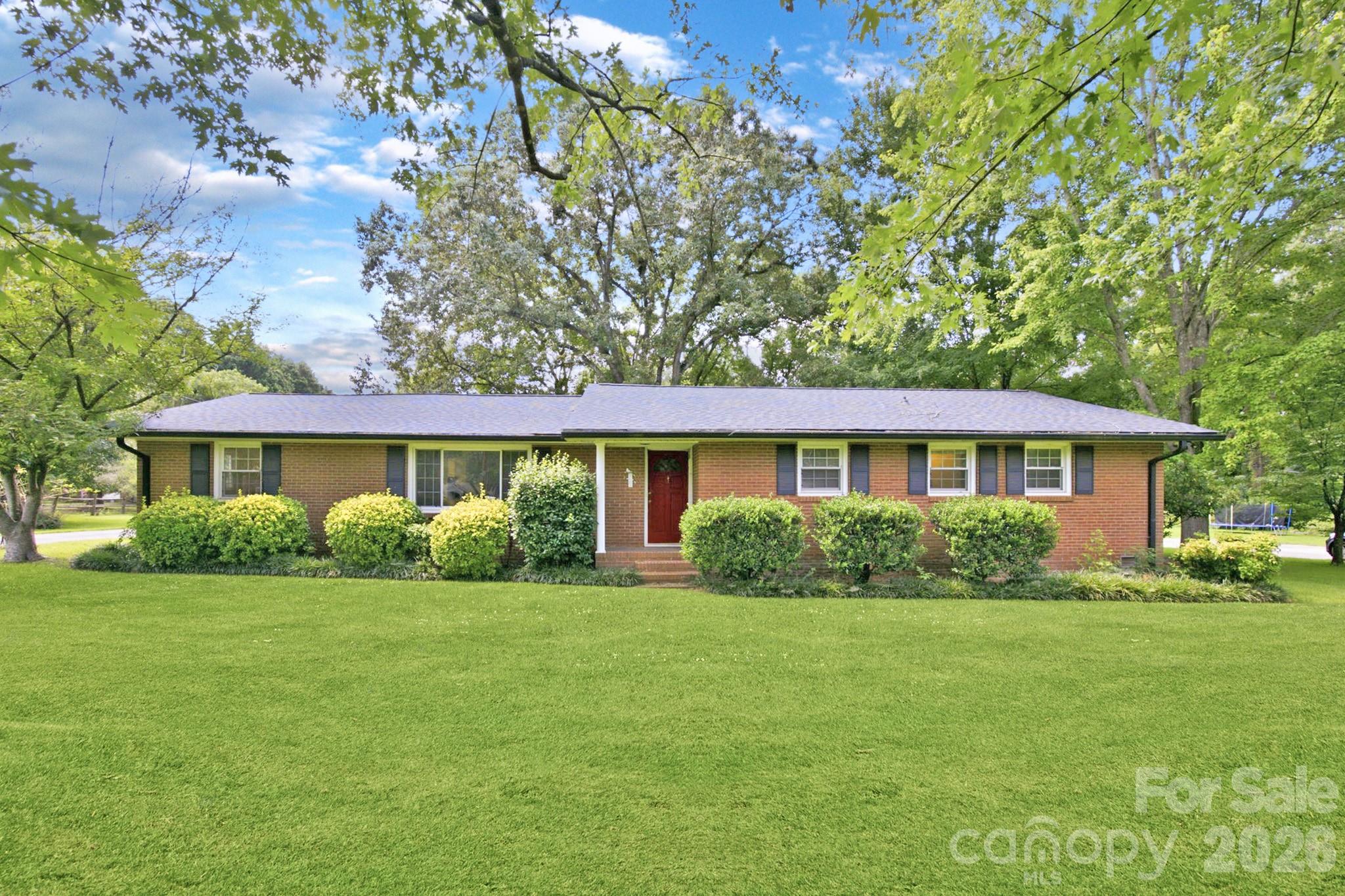 Set back on a private, wooded .67-acre lot in a sought-after Matthews location, this full-brick ranch is full of potential and ready for its next chapter. A long driveway leads through mature trees to the home, offering a peaceful, secluded feel. The home features 3 bedrooms, 2 full baths, and multiple living areas — including a cozy living room with a whitewashed brick fireplace and a spacious bonus/sunroom bathed in natural light, perfect as a home office, studio, or additional living space. Hardwood floors run throughout much of the home, and the kitchen overlooks a beautiful, private backyard. A detached two-car garage and storage shed add extra space for storage, hobbies, or workshop use. Enjoy the best of both worlds: a peaceful, wooded setting just minutes from shopping, dining, and major highways.
