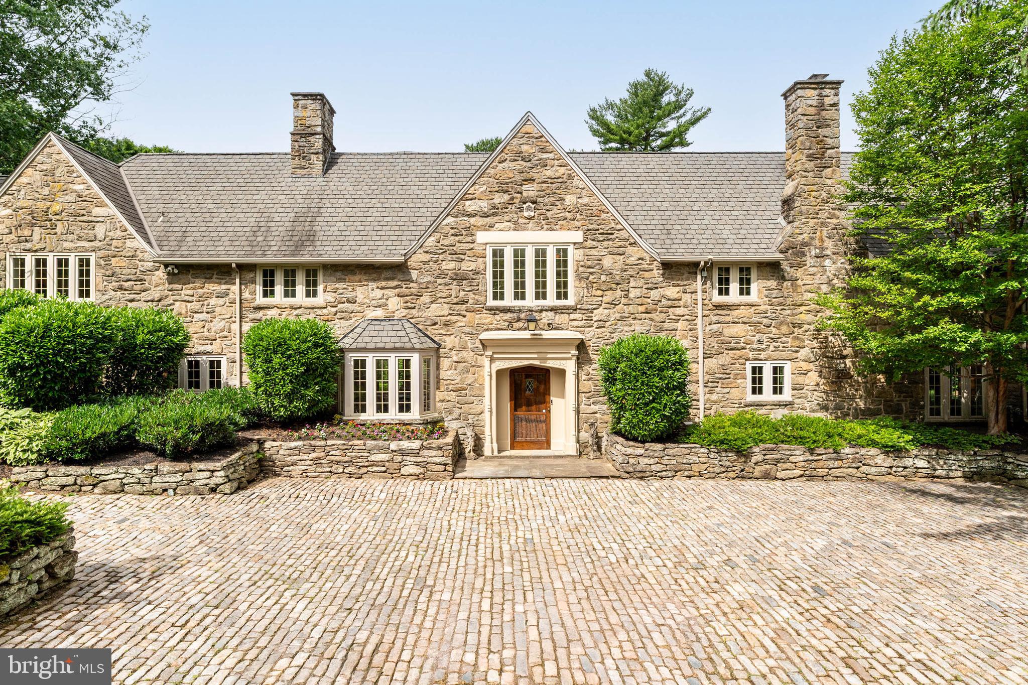 Set on one of Northside Haverford’s most prestigious lanes, this exceptional 1918 all-stone English Cotswold residence, designed by noted architect Walter Durham, blends timeless architecture with elegant living spaces and beautifully maintained grounds in a premier Main Line location.Approached from the street through an impressive Belgian block courtyard and driveway, the home immediately conveys classic sophistication and architectural presence. A gracious foyer welcomes you inside and opens to beautifully scaled formal spaces designed for both entertaining and everyday living.To the right, the elegant living room features a fireplace, beautiful bay windows overlooking the impressive grounds, and direct access to the rear flagstone patio. Adjacent is a distinguished wood-paneled library with its own fireplace, creating a warm and refined retreat. A conveniently located main-level powder room serves this wing of the home.The bright formal dining room is filled with natural light through expansive five-window arrangements overlooking both the front and rear grounds and flows seamlessly into the gourmet chef’s kitchen. Designed for serious cooking and gathering, the kitchen features a Vulcan commercial-grade oven, Sub-Zero refrigerator, and stunning honed Calacatta Gold marble countertops. A practical mudroom, abundant closet space, and a full bathroom conveniently positioned for outdoor entertaining and pool use complete the first floor.Upstairs, five spacious bedrooms and four full bathrooms provide exceptional accommodations. The luxurious primary suite offers peaceful views over the landscaped grounds, a separate alcove with custom built-in cabinetry, additional built-ins throughout the dressing and closet areas, and a private primary bath featuring double sinks and an oversized shower. A full room-sized upper-level laundry room and convenient rear staircase add functionality and ease to daily living.Additional highlights include hardwood floors throughout, multiple zoned HVAC systems, and a full-size basement offering abundant storage and flexibility.Outside, the property continues to impress with beautifully landscaped grounds featuring mature trees,  garden beds, and exceptional privacy. Tucked away from view, the lovely pool and pool area create a serene retreat surrounded by lush landscaping—an ideal setting for relaxing, entertaining, and enjoying the beauty of the seasons. Outdoor spaces are thoughtfully designed to offer both elegance and seclusion. Two separate garages complete this remarkable offering.Ideally located just moments from Merion Cricket Club and offering exceptional convenience to the best of the Main Line, this home provides easy access to Bryn Mawr, Villanova, township parks, Center City Philadelphia, Philadelphia International Airport, and major commuter routes while maintaining the privacy and prestige of one of Haverford’s most sought-after neighborhoods.A rare opportunity to own a distinguished Walter Durham-designed estate where historic character, exceptional craftsmanship, and elegant living come together.