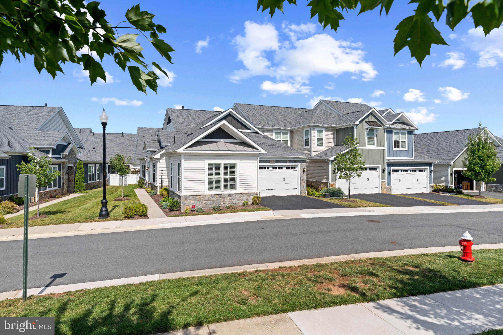 Welcome to 23702 September Sun Square, a beautiful residence in Birchwood at Brambleton, Loudoun County’s award-winning 55+ active adult community. Built in 2022, this like-new, end unit carriage house has the spacious feel of a single-family home paired with relaxed simplicity of main level living and ease of maintenance. Offering 2,406 sq. ft. of finished living space this home faces peaceful common grounds with ample guest parking–providing privacy, rich, natural light, and premium upgrades inside and out.The home is professionally landscaped with an integrated irrigation system, and a backyard oasis complete with a custom flagstone patio, knee-wall and covered retreat.Inside, the open concept, main level is bathed in natural light, characterized by 10 foot ceilings and oversized 8 foot doors. Upgraded flooring, lighting, and custom Norman-brand shutters flow throughout the home, creating an immediate sense of clean, sophistication. The well-appointed kitchen features a center island with premium quartz countertops, white shaker cabinetry, a deep stainless steel sink, gas cooktop, and microwave/wall oven combo around the center island. The kitchen flows seamlessly into the light, filled dining and gathering room, anchored by a striking linear stone, gas fireplace—perfect for all seasons and everyday comfort. The main level primary suite serves as a private sanctuary featuring an expansive walk-in closet and a spa en suite bath with custom oversized tile shower. Two additional main level rooms offer incredible versatility—one serves as a private guest suite with an attached full bath, while the third, separated by French doors, is perfect for a maker space, den or executive home office. Another full bath is available for guests on the main level and a convenient main level laundry room finishes the floor. Upstairs, a spacious 19‘ x 11‘ great room offers flexible space for a media lounge, hobby studio or secondary living spaceEnjoy smart home convenience with app controlled access as well. The home is equipped with a pre-wired Vintage Security system, featuring a central wall control panel with direct emergency dispatch capability; and a Ring security camera for added peace of mind. The two-car garage features a secondary refrigerator, abundant space for storage and a dedicated 240 V level two outlet, perfect for fast, charging EV and plug-in, hybrid vehicles.Living in Birchwood means being a part of a vibrant resort style living lifestyle with access  to world-class community amenities. Your HOA fee covers comprehensive lawn care and yard maintenance, high-speed internet, cable TV, trash and snow removal, and full access to two clubhouses, a full scale calendar of social events, clubs and resident led activities, and all resort-style community amenities. Birchwood amenities include: —Indoor and outdoor pools;—State-of-the-art fitness centers;—Golf simulator;—Pool Table;—Art room;—Pickleball and bocce courts;—Scenic walking trails; and—Community Garden.Located just minutes from premier shopping, dining, top tier medical facilities, major commuter routes and Dulles International Airport, this home is ideal for 55+ active listing, offering the perfect blend of luxury, convenience and community.
