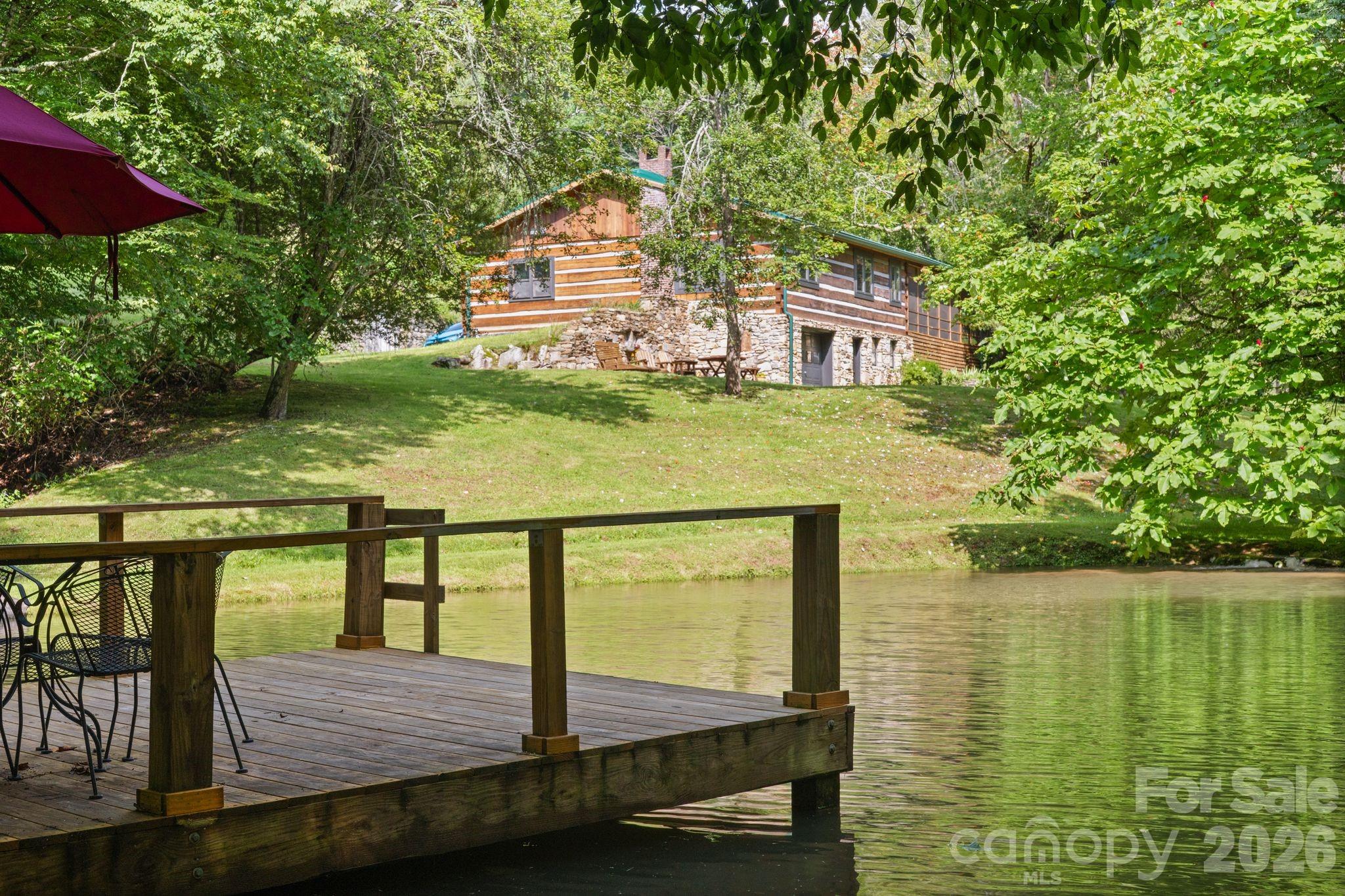 Tucked away 40 minutes north of Asheville, this extraordinary 35-acre sanctuary at 1061 Indian Trail is a true Appalachian homestead rich with character and heritage. Having known only three owners throughout its history, the estate offers an irreplaceable sense of place, completely surrounded by the pristine, protected wilderness of Pisgah National Forest. Accessed via a scenic Forest Service gravel road, the land transitions from lush timber to roughly 10 cleared acres complete with an organic garden, mature muscadine vines, and producing blueberry bushes. The native wildlife creates an enchanting backdrop, with regular sightings of bald eagles, black bears, and rare fireflies. Flowing from above the property onto and through the land, Hampton Creek cascades down to a waterfall that can be heard right from the house before making its way to the private trout pond, which features a small dock with a ladder for easy swimming and kayaking access.The main residence is thoughtfully designed to showcase the idyllic surroundings. It features three bedrooms and three bathrooms, including main-floor bedrooms that look directly out over the calm waters of the pond. Two of the main-level bathrooms have been recently renovated, blending modern comfort with mountain charm. Below, the basement provides extra flexible space complete with a third full bathroom, a newly finished bonus room, and abundant storage space. The heart of the home extends outdoors to a sweeping, screened-in wraparound porch that captures the crisp mountain air, alongside a convenient attached single-car carport. Nearby, a historic root cellar built directly into the hillside offers a fascinating nod to traditional mountain living.A second home on the property—a light-filled guest cabin with a proven track record as a successful short-term rental—provides flexible living options or instant income potential. The cabin features a smart, two-story layout with an open-concept kitchen, living area, and half bath upstairs, while three bedrooms and a full bathroom rest quietly on the lower level. Its private porch sits nestled in the canopy, offering another elevated view of the trout pond and an additional equipment shed nearby to store farm or lawn gear.Beyond the property line, outdoor adventure is practically infinite. The iconic Appalachian Trail is located just a short distance away, while nearby Wolf Laurel and Hatley Point provide exceptional resort amenities, including golf, tennis, dining, and fitness facilities. Hatley Point also features a newly renovated lodge, winter skiing, and a new mountain bike park. Offering a rare combination of complete privacy, rich history, and modern recreational convenience, this legendary mountain retreat stands ready for its next chapter.