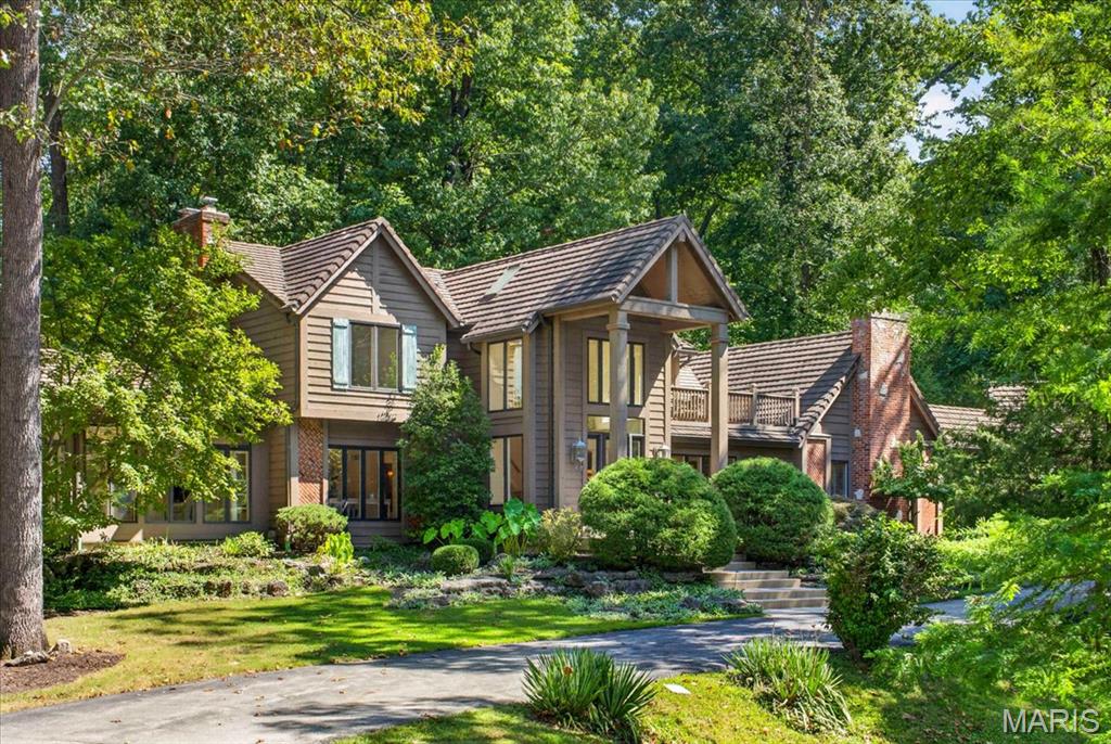 A truly special property where Tudor character meets resort-style living, tucked into a lush, wooded lot in one of the area's most private settings. This 4-bedroom, 3.5-bath home pairs a striking gabled façade, handsome brick accents and a richly textured shake-style roof with mature landscaping and a stacked-stone waterfall built into the hillside.Step inside to a soaring two-story foyer with a wraparound balcony, skylights and fluted columns. The great room features a brick fireplace and stained-glass transom windows — a detail that repeats throughout the home. French doors lead to a formal living room. The kitchen offers ornate custom cabinetry, solid-surface counters, a professional-grade range and a hand-carved butcher-block island, with a window over the sink framing the waterfall and pool beyond. A breakfast nook, a vaulted skylit sunroom and a main-floor laundry room finished with matching custom cabinetry round out the main level.The main-level primary suite includes its own gas fireplace and a spa-like bath: a corner soaking tub in a bay window, an oversized walk-in shower, dual vanities, a separate water closet and a stained-glass accent window. An exceptional walk-in closet boasts extensive custom built-ins, creating a beautifully organized dressing space with abundant storage. Upstairs, a second primary suite offers its own bath, dual closets and a private composite deck overlooking the grounds — ideal for guests or family.The finished lower level adds a spacious rec room and a custom wet bar with brass hardware and a mirrored back bar, built for movie nights and gatherings.Outside, a flagstone patio wraps a free-form pool, with the stacked-stone waterfall cascading into its own pond just steps away — all framed by mature trees and total privacy.The detached, heated 3-car garage connects to the home via a covered breezeway and hides a bonus: a finished upper loft with new luxury vinyl flooring, built-in storage and its own dedicated furnace — ideal as a home gym, hobby space or flex room. Central vacuum runs through both the home and garage.Architecturally distinctive and set on one of the most private lots around, this is a home that has to be walked through to be believed.