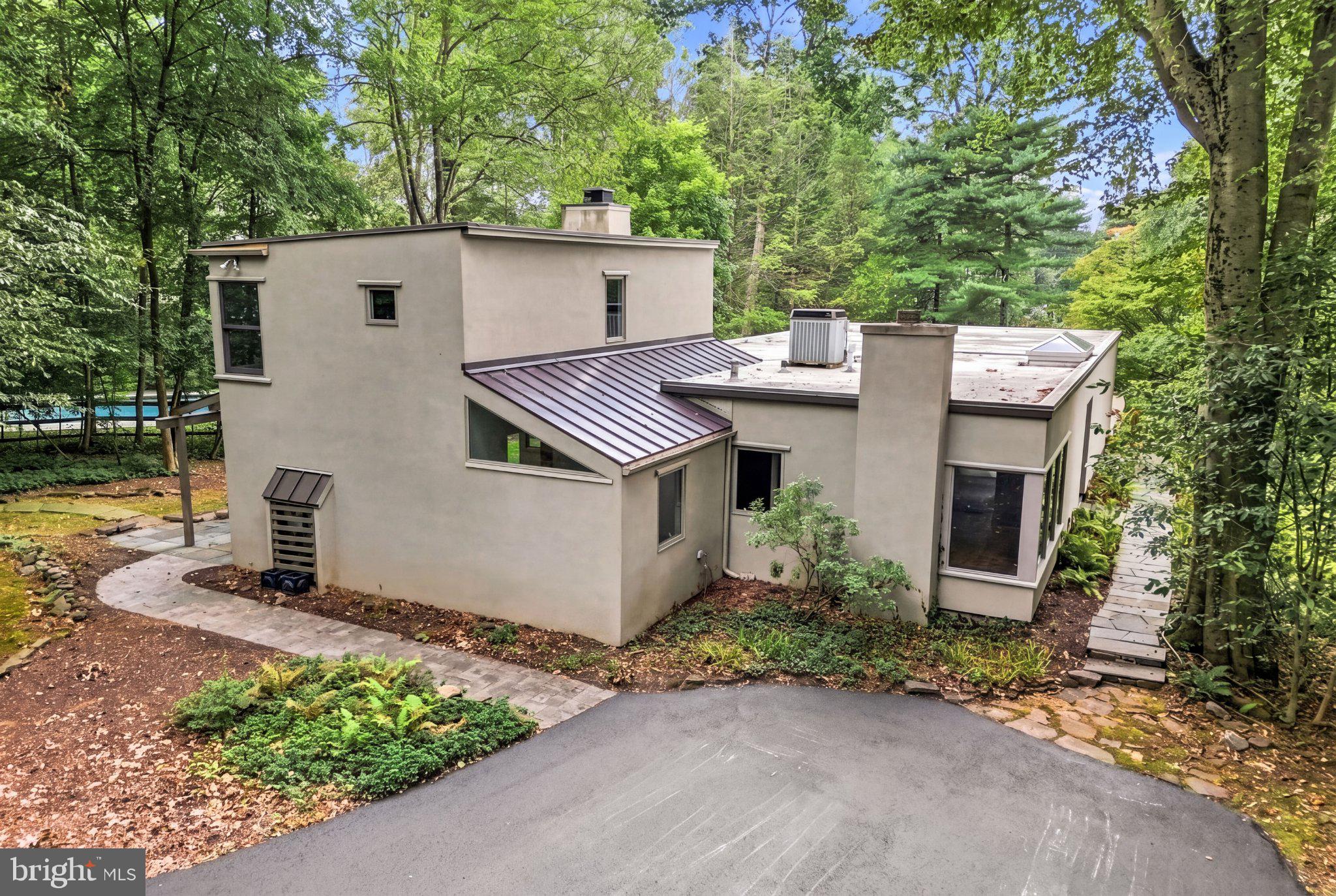 A rare opportunity to own one of Gladwyne’s most charming and architecturally intriguing homes, 815 Black Rock Road is filled with character, fascinating history and incredible potential. Set on just under an acre of flat, private grounds shaded by magnificent mature trees, the home was originally built around 1930 as a U.S. Steel prefabricated model home and was won at the Devon Horse Show. Later expanded with sensitivity to the original design, the residence combines clean geometric forms, curved walls, expansive glass and a wonderful connection to its natural surroundings. Ready for thoughtful updating, this is an exciting opportunity for a buyer who appreciates a cool, character-filled home and wants to put their own stamp on something truly different.The light-filled entrance opens to a flexible main level where nearly every room offers views of the wooded grounds. The spacious living room features hardwood floors, a gently curved wall, gallery-style track lighting and multiple sets of glass doors opening to a large stone terrace. The adjoining dining room is equally inviting, with beautiful parquet flooring, a wood-burning fireplace and oversized corner windows that frame the mature trees beyond. These spaces flow easily from one to the next while still retaining their own personality and architectural interest.The kitchen offers abundant cabinetry, a Sub-Zero refrigerator, gas cooktop, multiple dishwashers and a Mercer tile backsplash that brings warmth, artistry and local character to the space. Just beyond, the dramatic sunken family room is surrounded by walls and a sloped ceiling of glass, creating the feeling of being immersed in the landscape. A second wood-burning fireplace anchors the room, while its open connection to the kitchen makes it a natural gathering place for everyday living and entertaining. A dedicated office area with built-in work surfaces and shelving, along with main-level laundry, adds convenience and functionality.Also on the main level is a bedroom and two full baths, as well as an additional flexible room that could serve as a fourth bedroom, private office, studio, playroom or entertaining space. This adaptable layout offers the possibility of primarily one-level living while still providing ample room for guests, work and hobbies. Upstairs, two bright bedrooms feature hardwood floors and corner windows overlooking the trees, and share a full hall bath.The outdoor setting is one of the property’s greatest assets. Expansive stone terraces, a pergola, level lawn and mature plantings create a peaceful backdrop for outdoor living. Tucked privately among the trees is a gorgeous swimming pool with an adjoining hot tub and a separate pool house designed for relaxed summer days and casual entertaining. The pool house includes a kitchen, full bath, storage shed, screened porch and a loft area that can provide additional storage or a fun play space for children.Rich in history, character and possibility, 815 Black Rock Road offers the chance to reimagine a truly special home in a beautiful Gladwyne setting. Just down the road from the heart of Gladwyne and conveniently located close to parks, schools, clubs, shopping, dining and major roadways, this special property offers privacy, flexibility and an opportunity that is difficult to replicate.