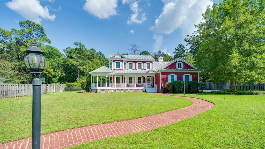 Full of character and custom details, this 2,356-square-foot two-story home offers 4 bedrooms, 2 full baths, and 2 half baths with a layout that combines comfortable everyday living with plenty of space to spread out. A welcoming covered front porch, brick walkway, mature landscaping, and classic architectural details create standout curb appeal. Inside, the main living area features beautiful hardwood floors, a fireplace, soaring ceilings, abundant natural light, and an open staircase with detailed woodwork overlooking the space below. The kitchen offers generous cabinet and counter space, a large peninsula for additional prep or seating, and an adjoining dining area, while the light-filled rear sunroom provides another inviting place to relax and enjoy views of the backyard. The primary suite is conveniently located on the main level and includes a walk-in closet and private bath with double-sink vanity. A separate laundry room adds everyday convenience and keeps household tasks tucked away from the main living spaces. Outside, the spacious fully fenced backyard is made for enjoying, with two large back decks offering plenty of room for grilling, entertaining, or relaxing outdoors, along with a covered patio and mature trees that provide shade and character. The property backs up to plantation land, giving the backyard an added sense of privacy with no neighboring homes directly behind the property. Additional features include a two-car garage, a detached insulated building with a roll-up door that is ideal for a workshop, hobby space, equipment storage, or other uses, plus a separate smaller matching woodworking shop for even more versatile workspace and storage. With its distinctive custom design, generous indoor and outdoor living spaces, private setting, and impressive collection of extras, this home offers a combination of charm, functionality, and space that is hard to duplicate. Schedule your private showing today and come see everything this one-of-a-kind property has to offer!